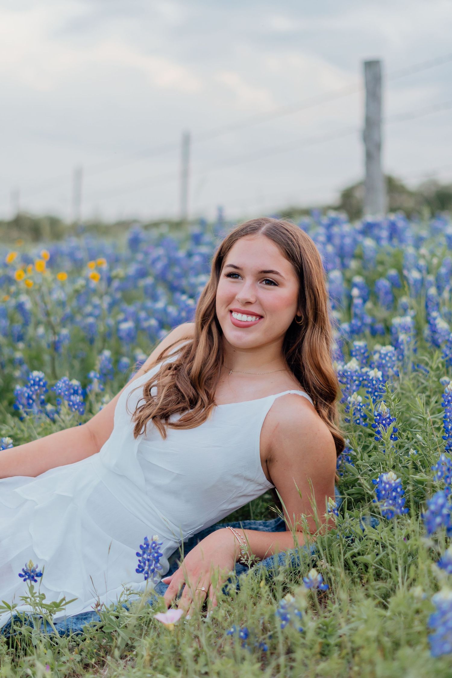 Someone poses elegantly among blooming bluebonnets in a white dress during a spring photoshoot.