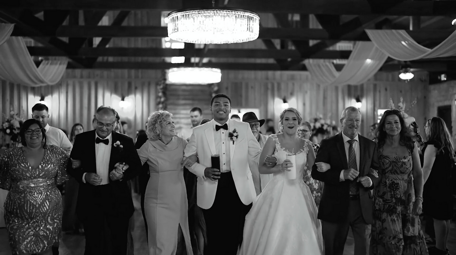 Black and white panorama of a lively wedding reception with guests dancing on the dance floor.