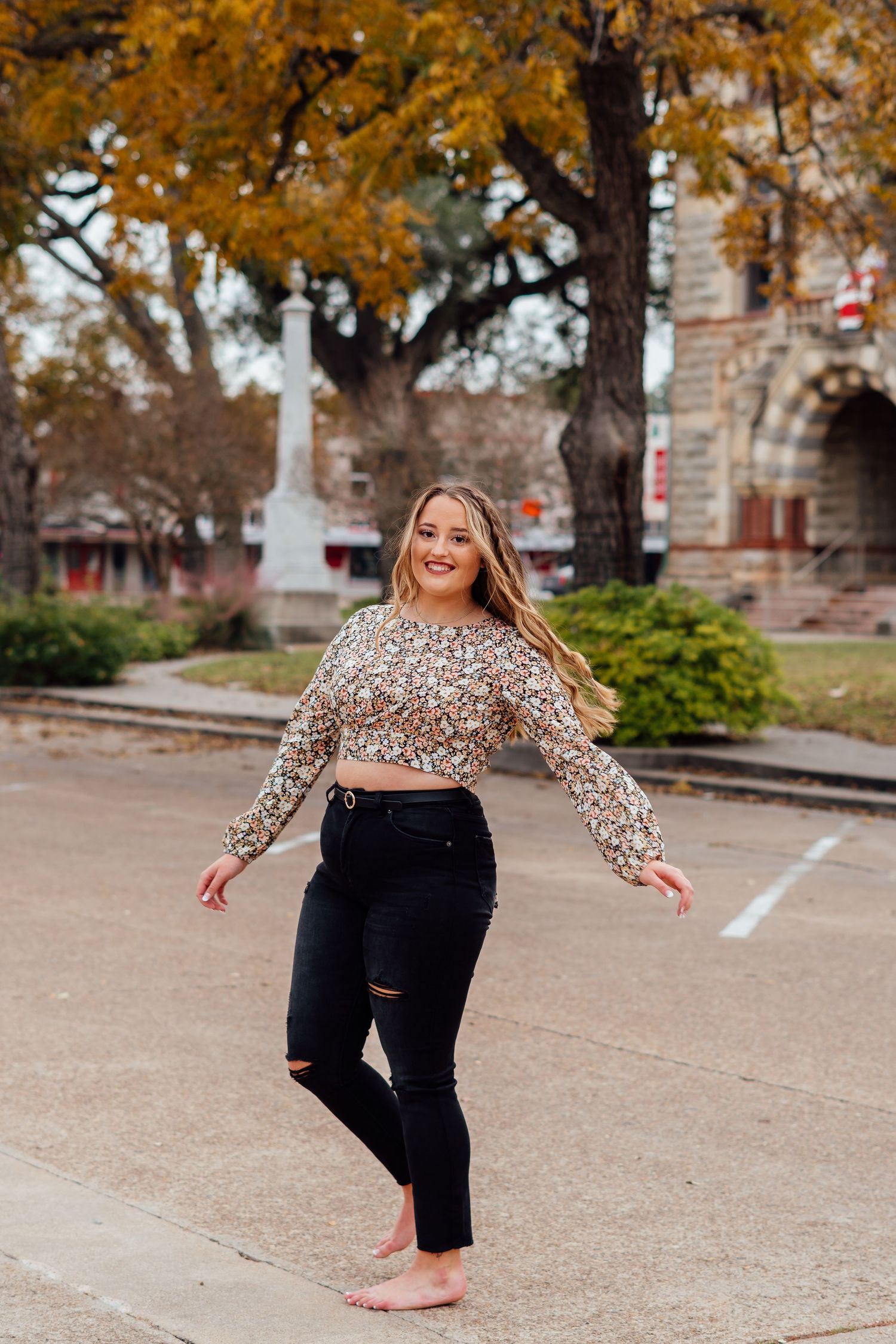 Dancing poses in sparkly top and black pants on outdoor pavement with fall foliage.