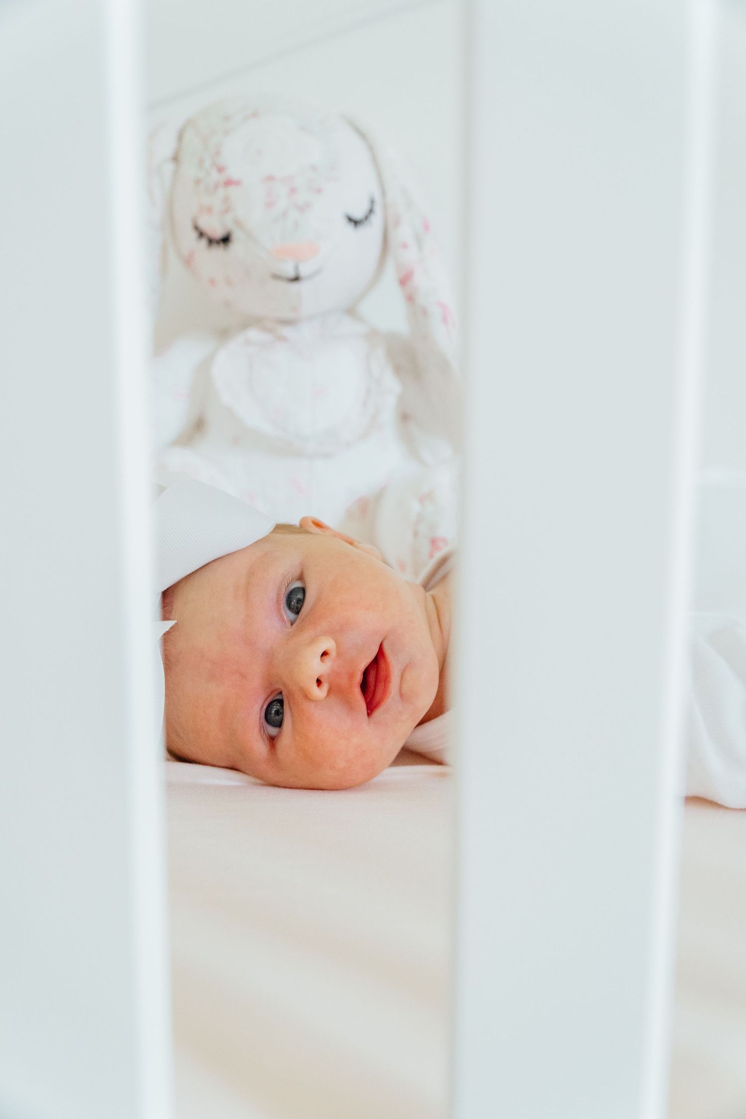 Close up of baby peeking through white crib slats in nursery.