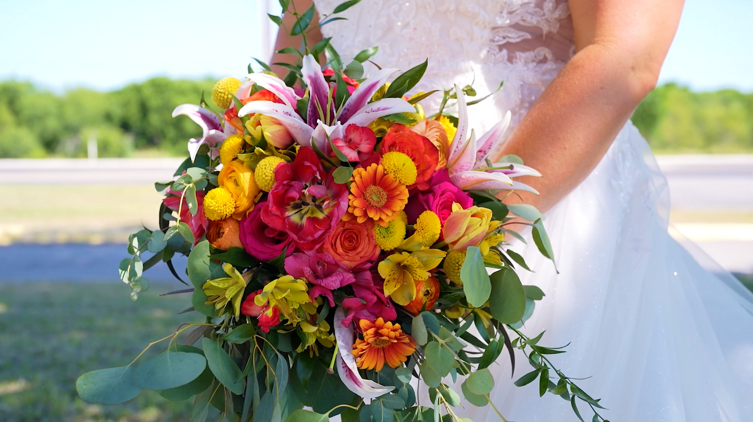 Vibrant floral arrangements featuring yellow, orange and pink blooms with greenery line an outdoor venue.