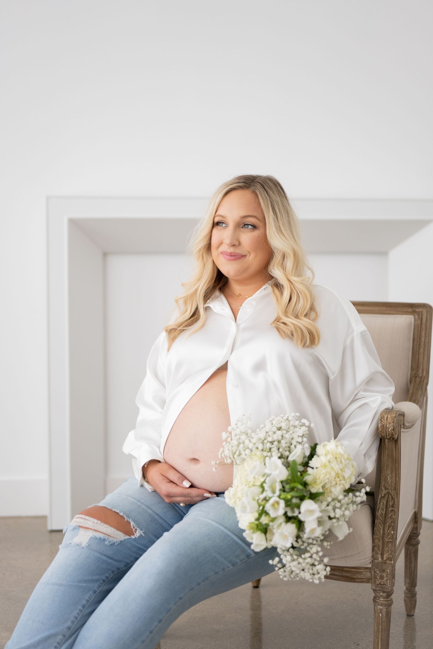 Maternity photo session with woman in white shirt and jeans sitting with baby's breath flowers.