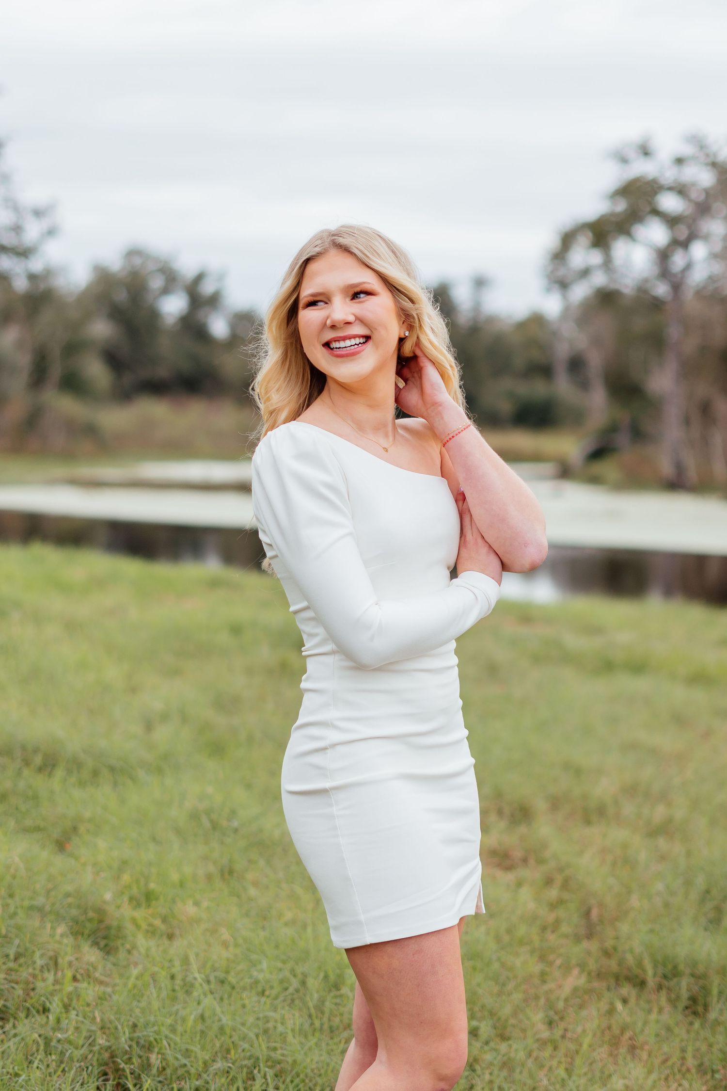 Outdoor portrait session in white dress on grassy field near water.