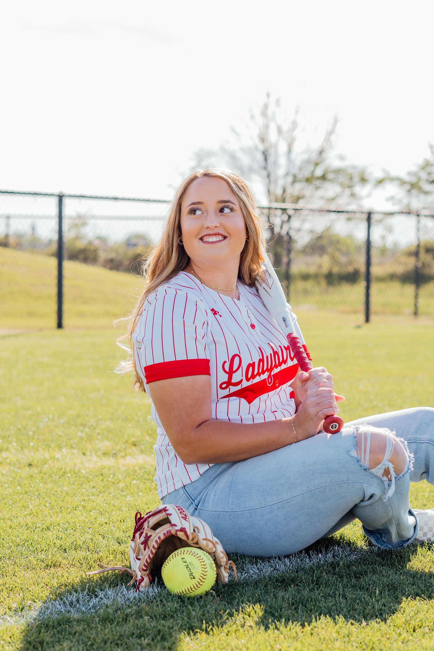 Softball themed photo shoot with player resting on grass field.