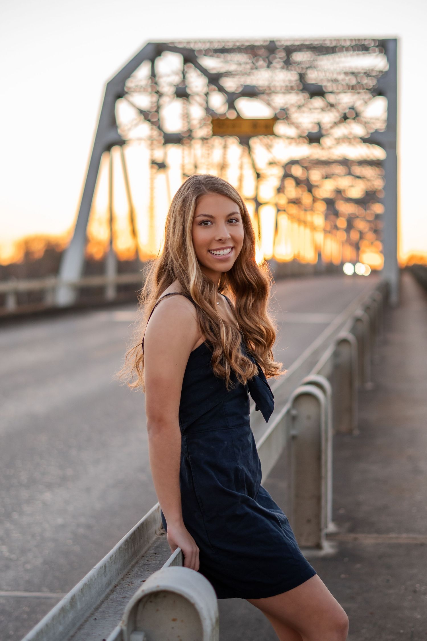 Casual sunset photoshoot on a bridge with industrial backdrop.