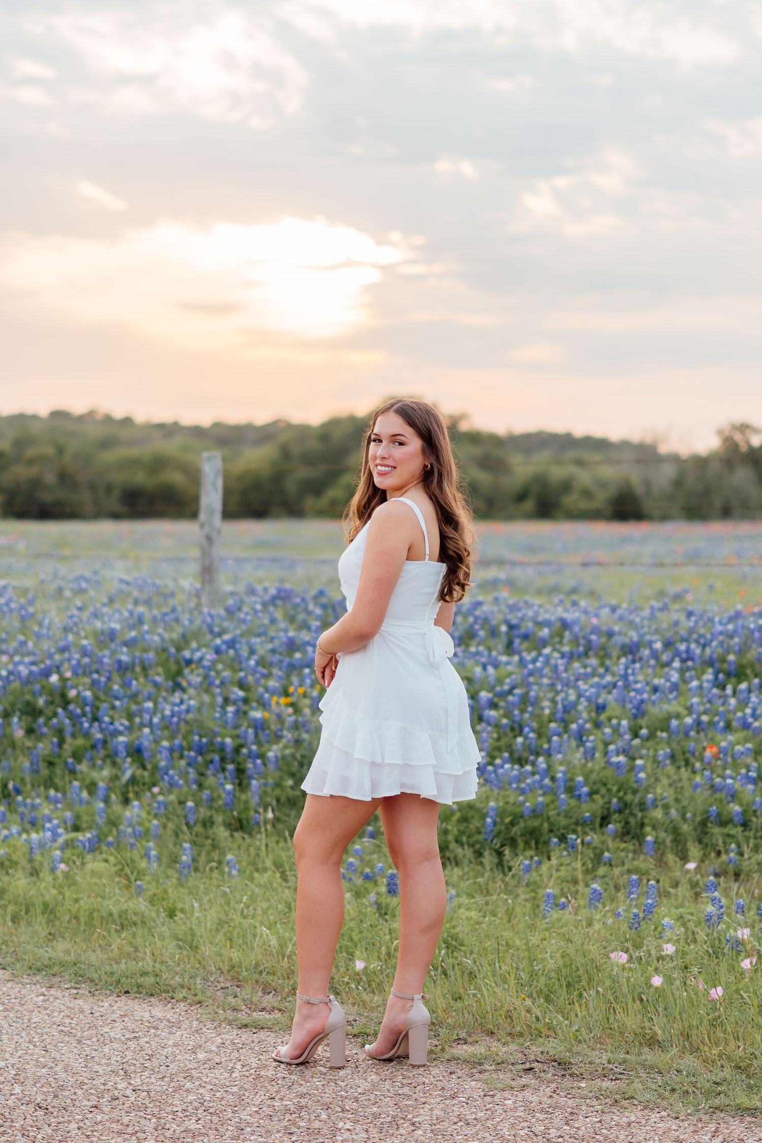 A photoshoot in a field of Texas bluebonnets during sunset wearing a white dress.