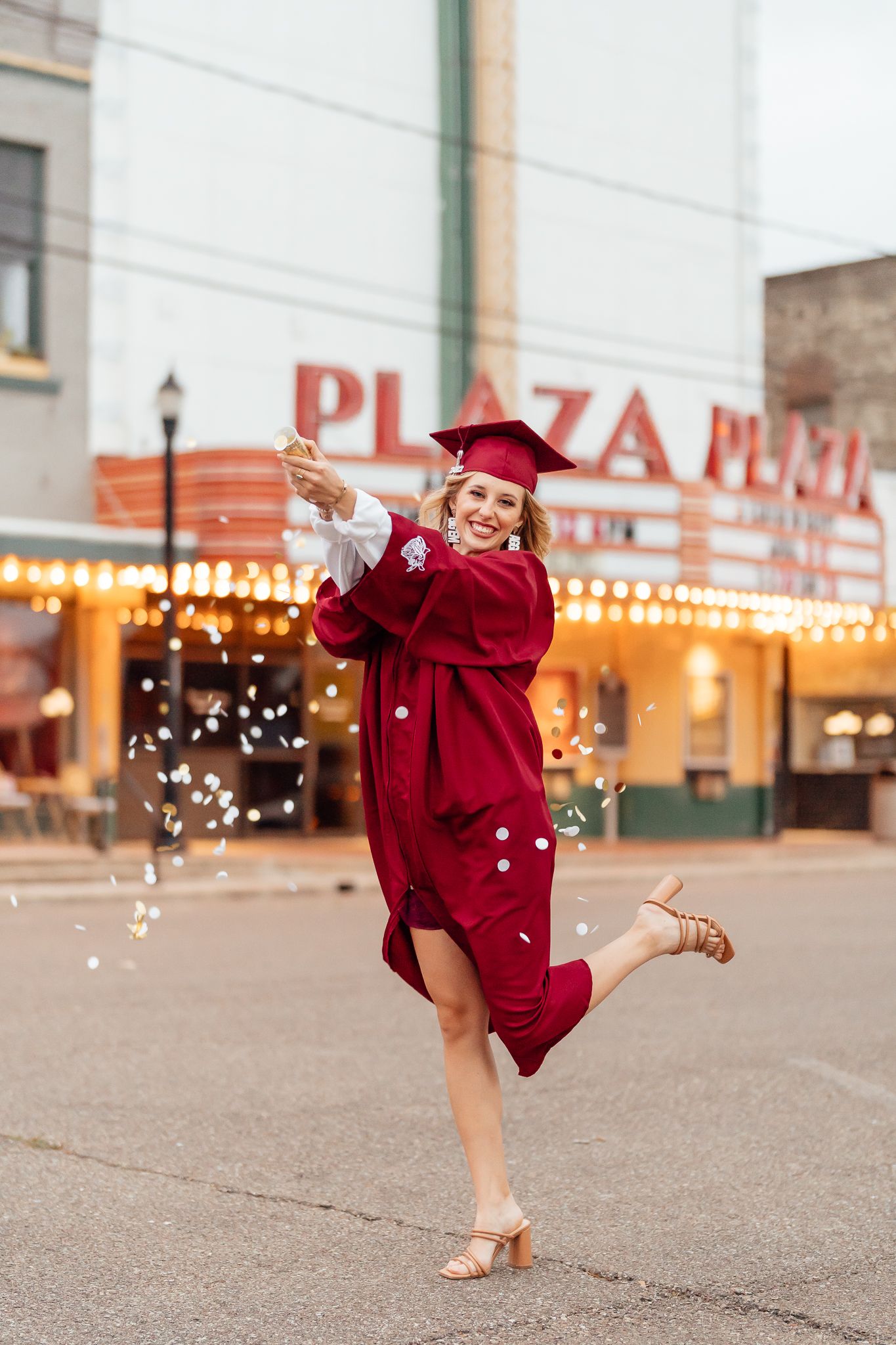 Person in a red graduation gown twirling outdoors in front of a plaza.