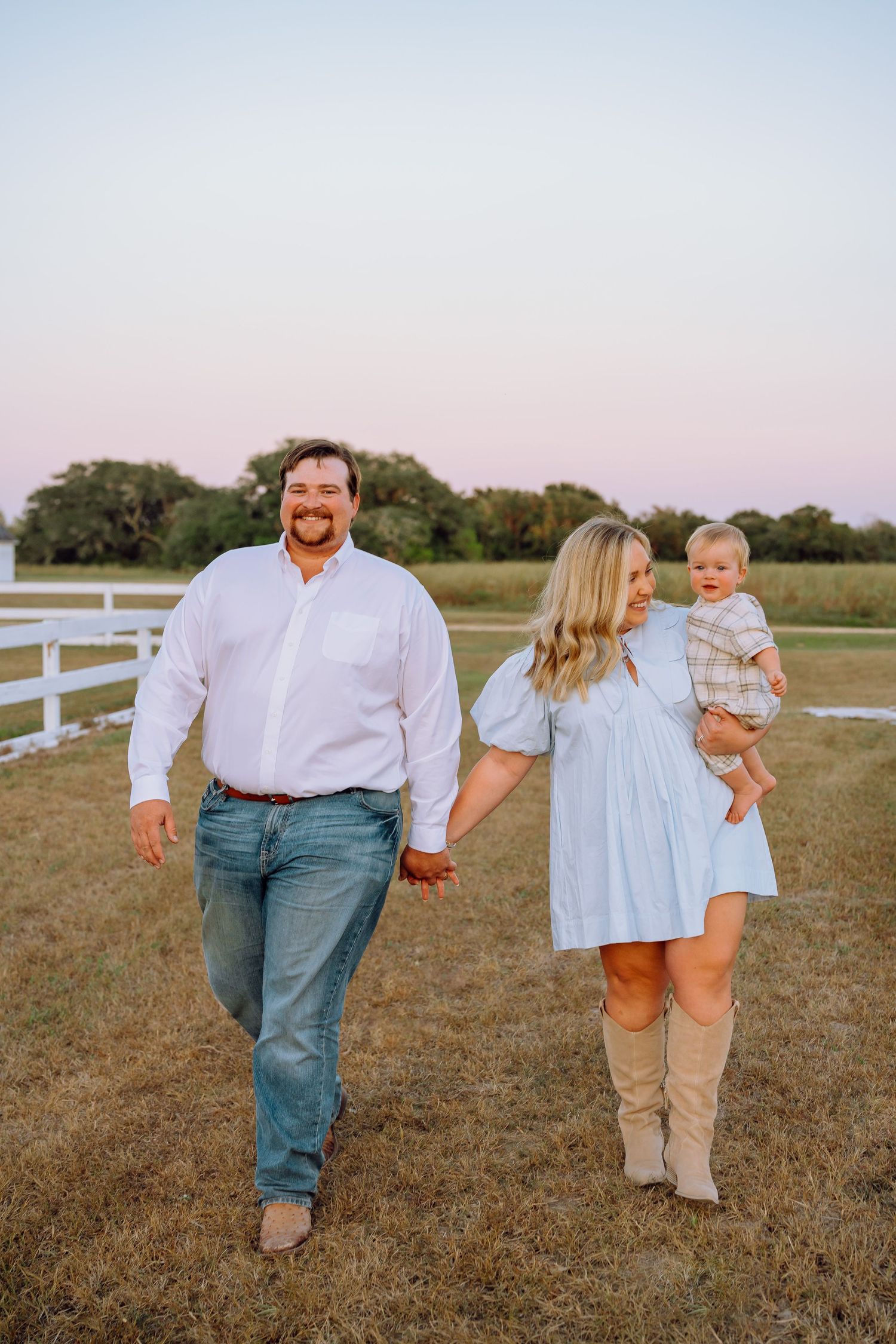 Family walks together through a grassy field during golden hour photography session.