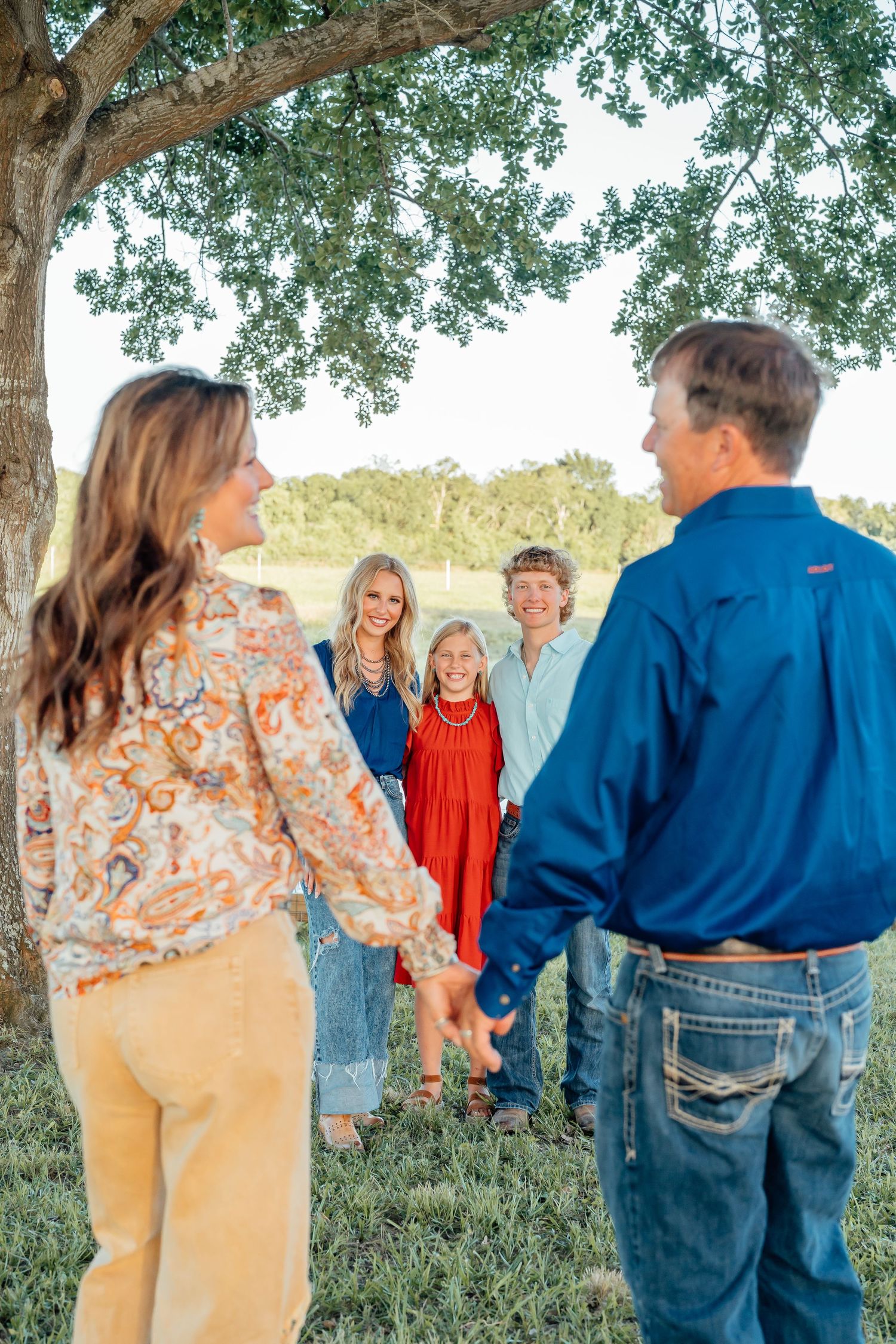 Family members walking together under shade trees in casual outdoor setting.