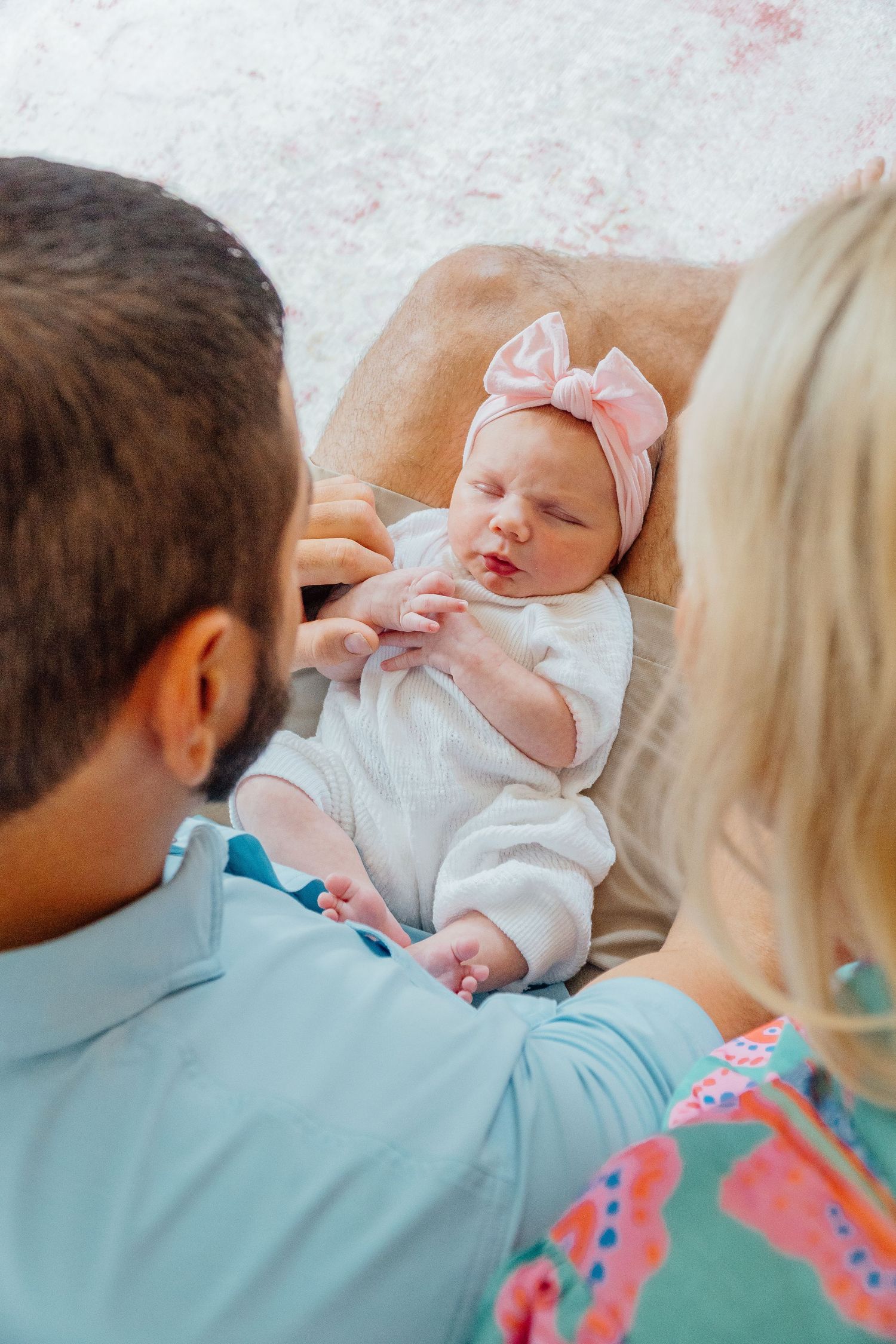 Newborn baby wearing white outfit and pink bow during intimate family moment.