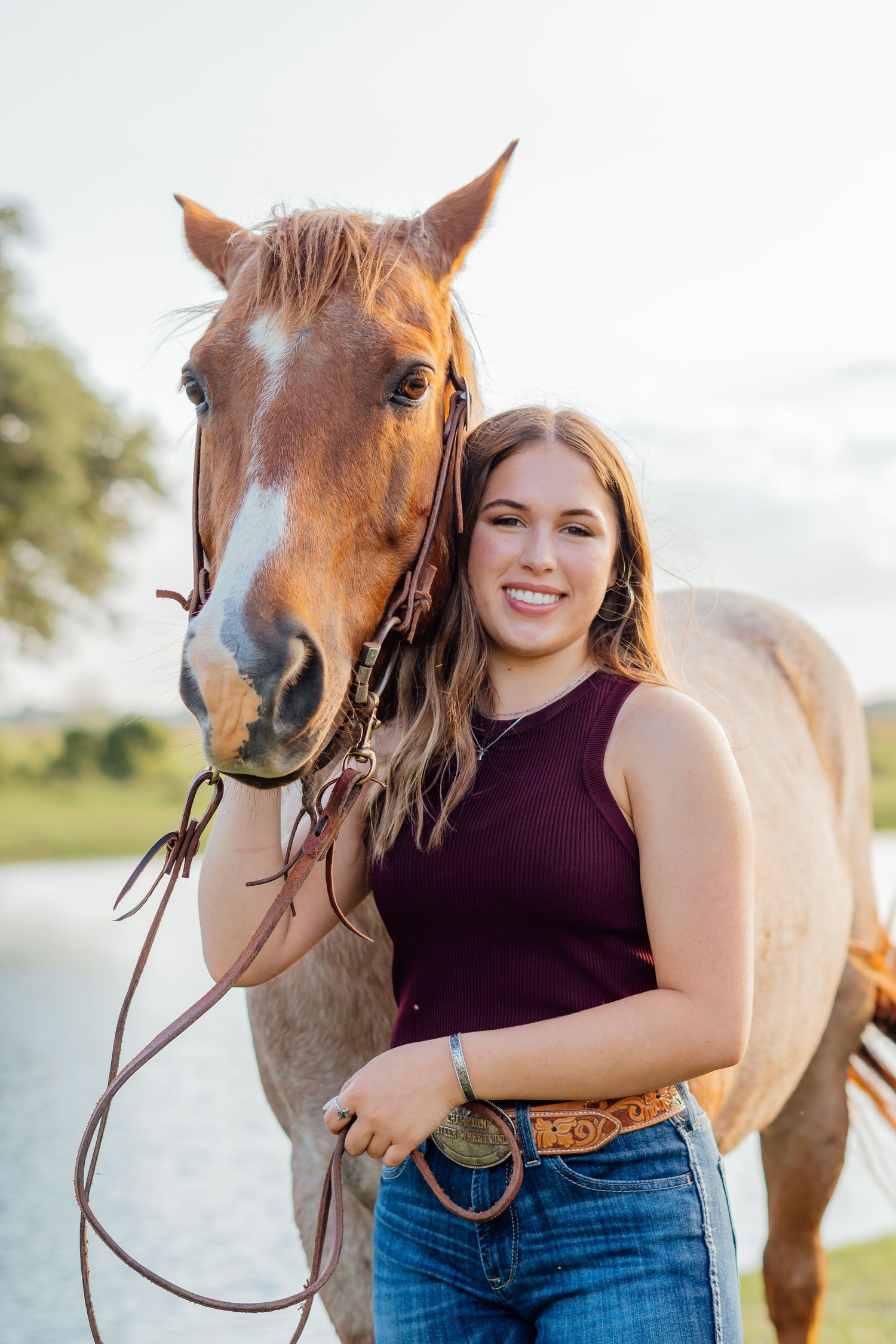 Outdoor portrait with friendly chestnut horse wearing purple tank top and jeans.