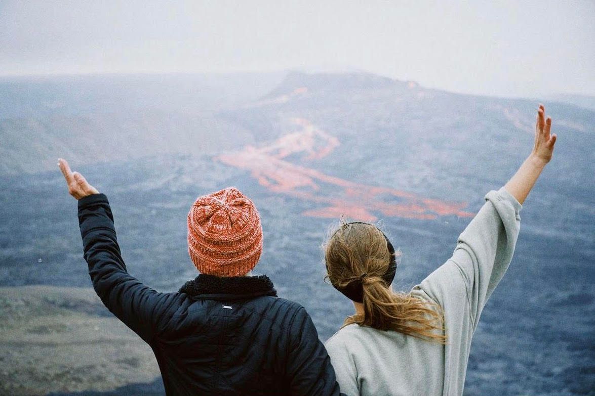 People with raised arms celebrating on mountain overlook at sunset.