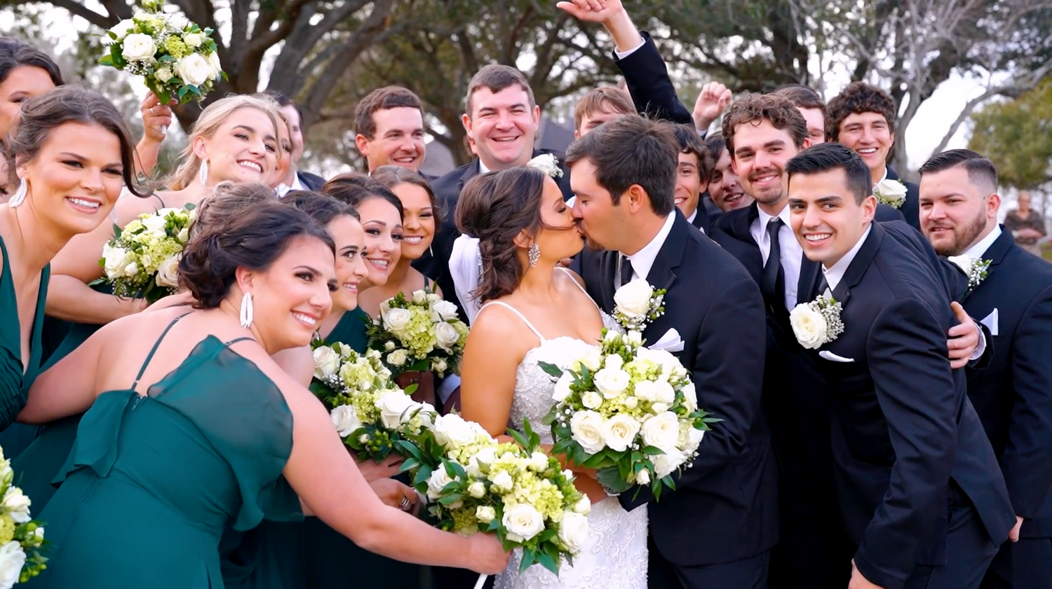 Outdoor wedding celebration with guests smiling and laughing in formal attire.