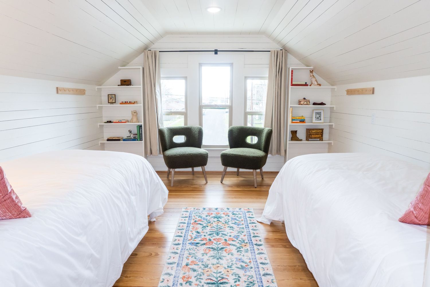 Bright attic bedroom with white walls, hardwood floors and colorful accent textiles.