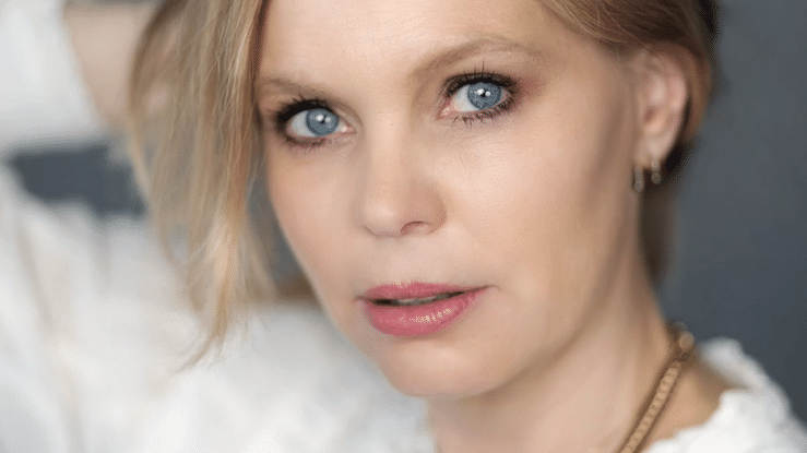 A close-up portrait with striking blue eyes and soft blonde hair against a light background.