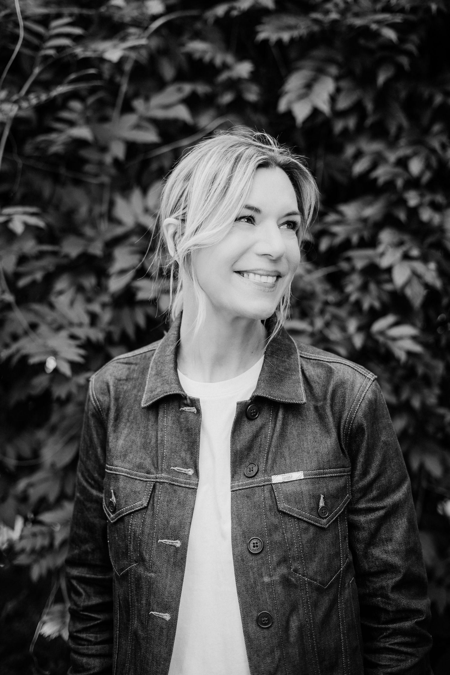 Black and white portrait wearing denim jacket with leaves in background.