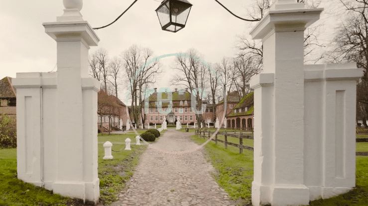 A gravel path leads through white gates and pillars into a historic cemetery with gravestones and trees.