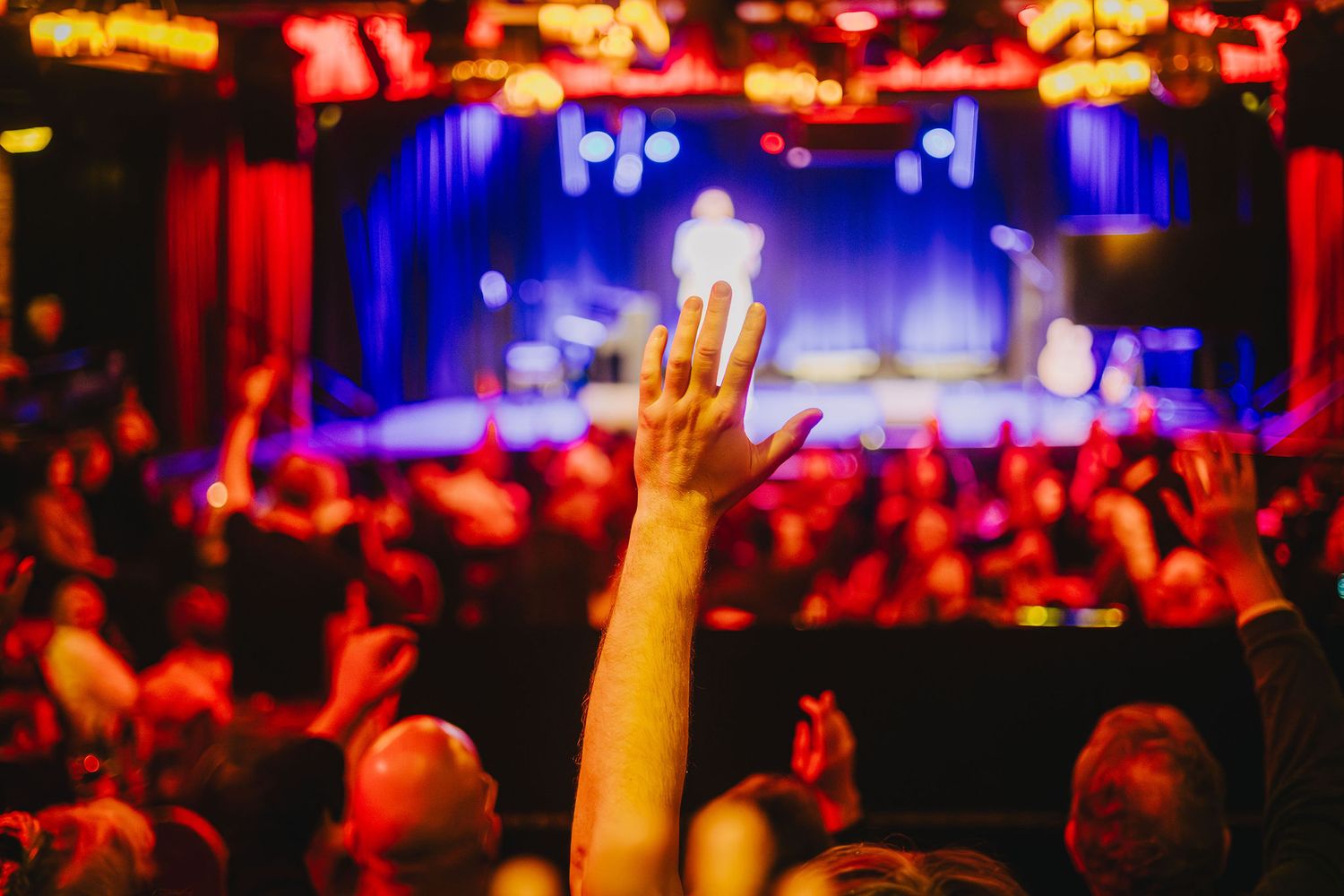 Concert crowd with raised hands illuminated by red and blue stage lights.