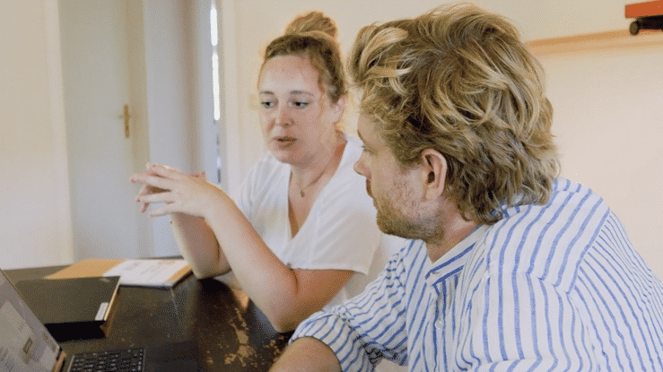 A group of people in a casual office setting collaborate around a table during a meeting or discussion.