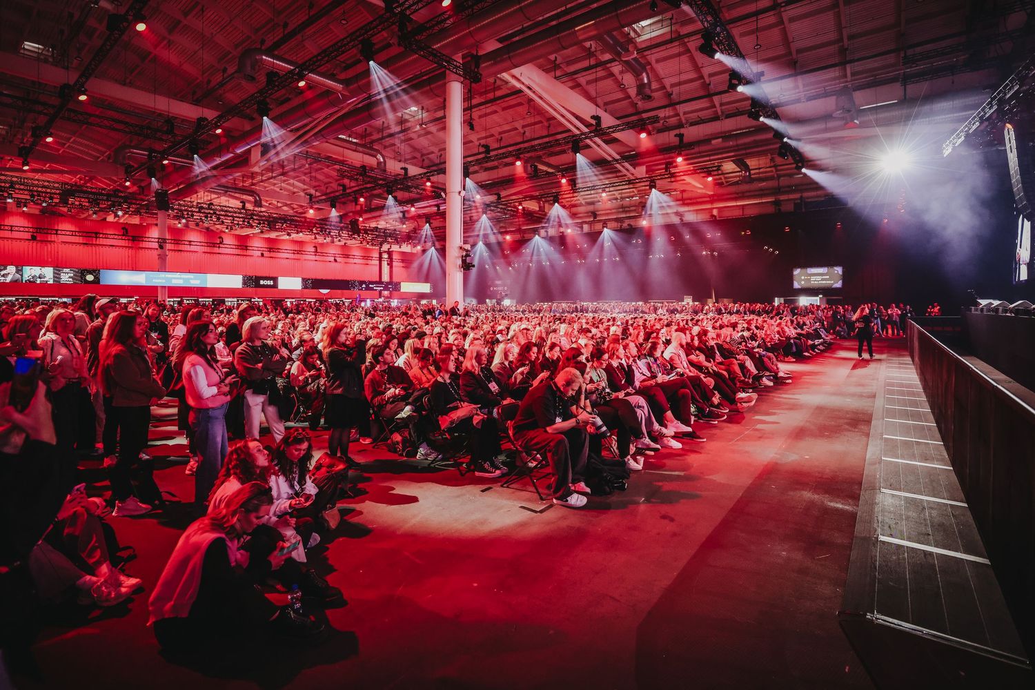 Large audience event space illuminated with dramatic red lighting and fog effects.