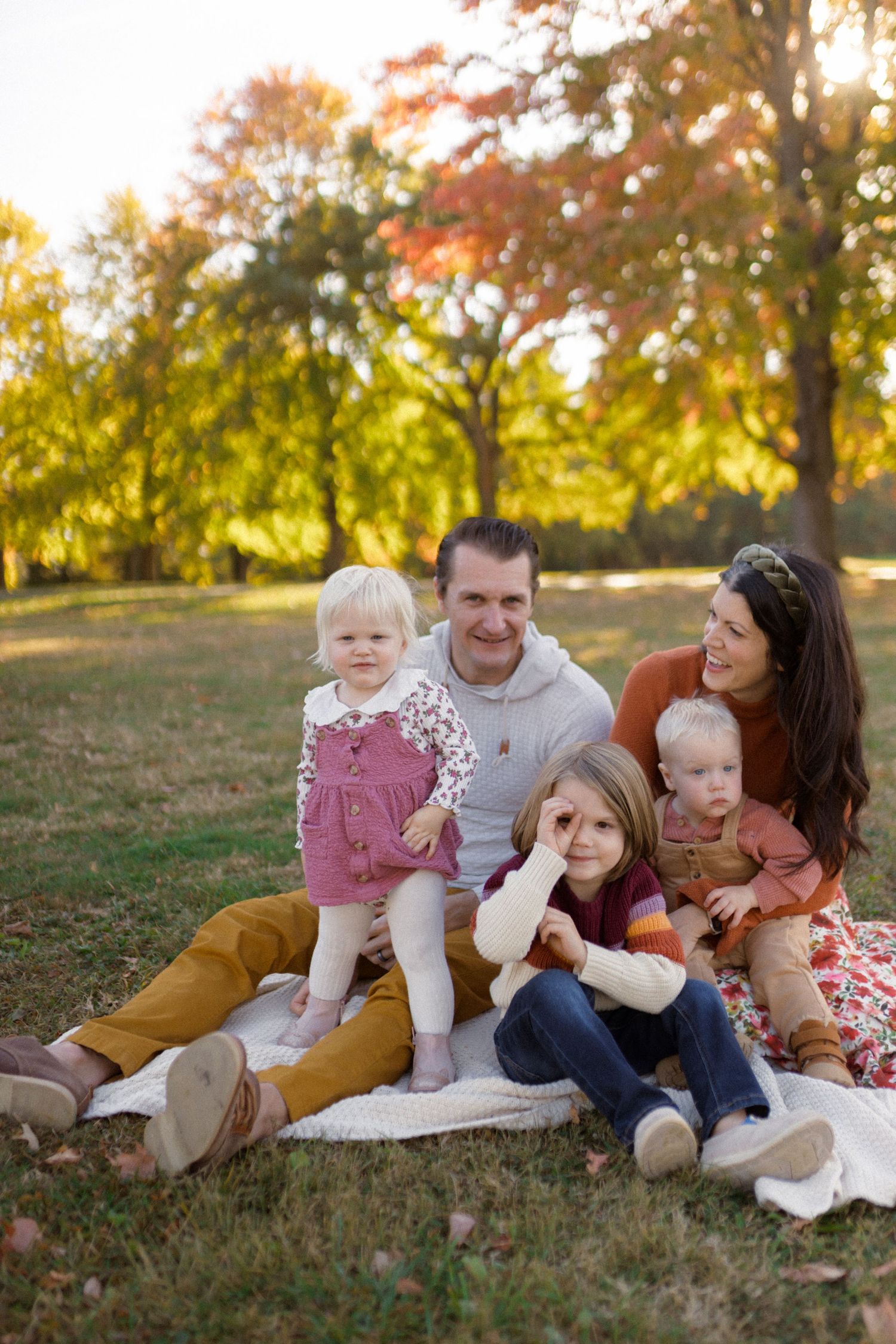 Family with three kids sitting on a blanket in a field in a natural, candid, manner.