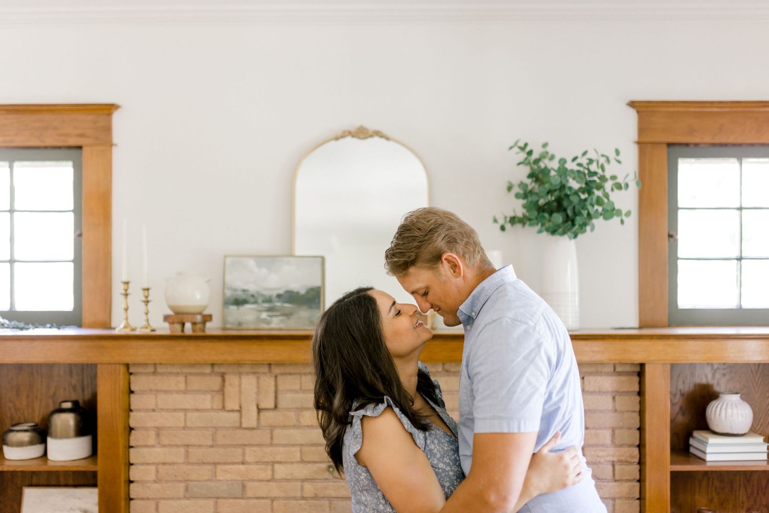 Intimate photo of a couple smiling, about to kiss in their home in front of a fireplace