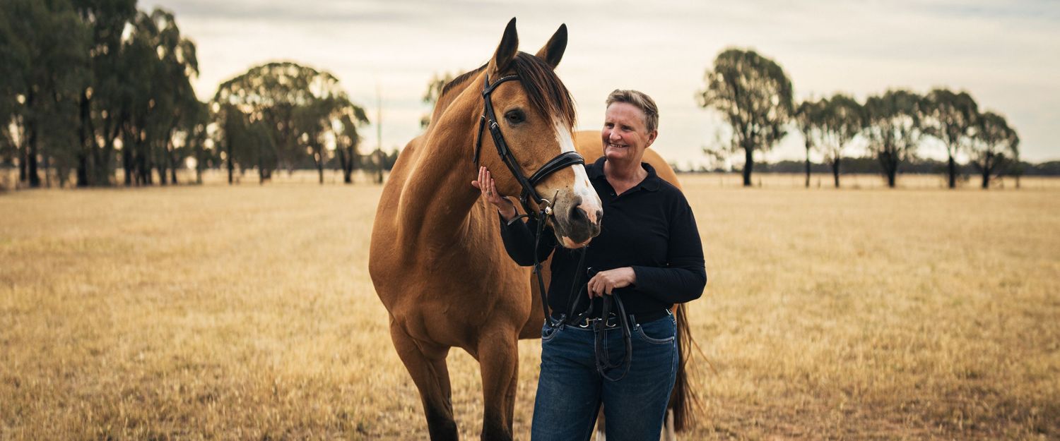 A woman posing with her horse in a rural paddock during a relaxed portrait session.