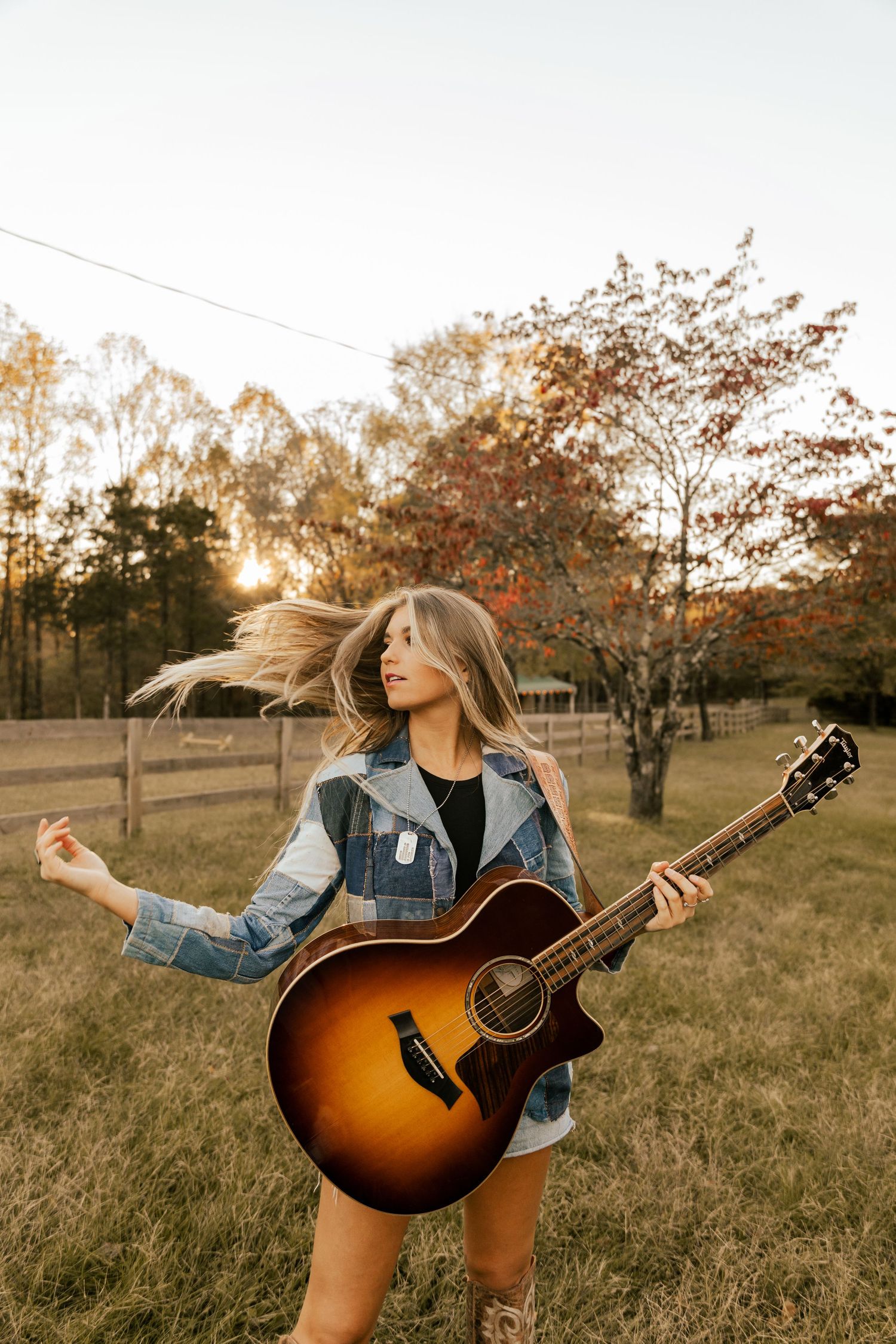 Nashville artist Brennley Brown playing acoustic guitar in autumn field at sunset wearing denim jacket.
