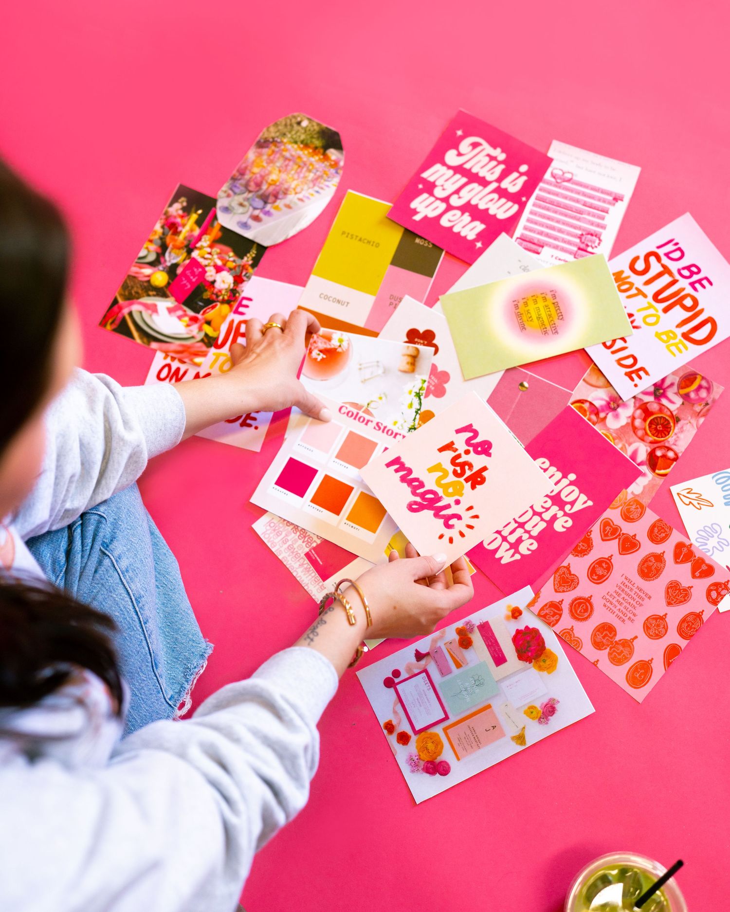 Hands arranging colorful pink and red design materials on a bright background.