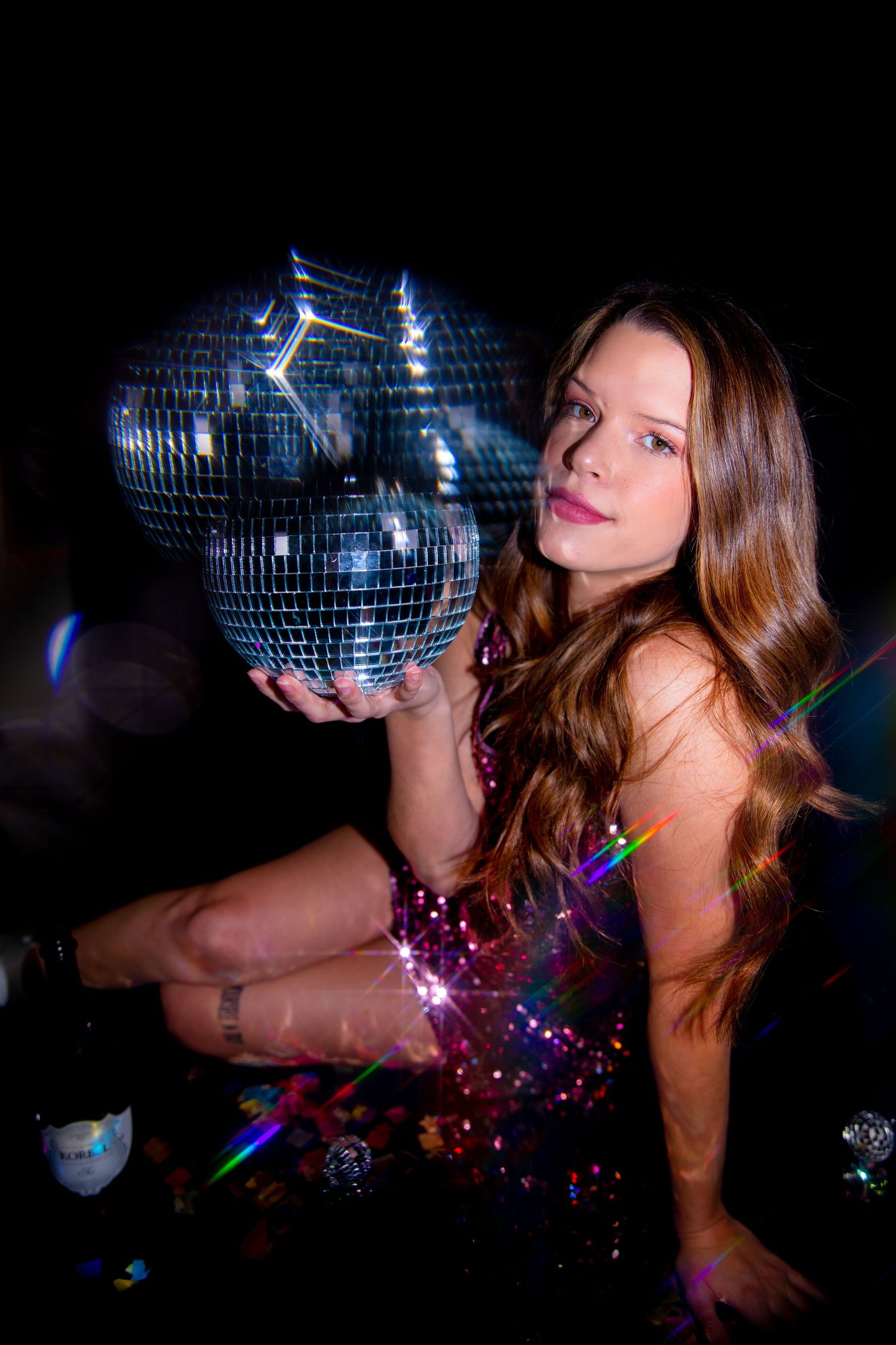 Glamorous disco ball photoshoot in dark room with dramatic lighting effects.