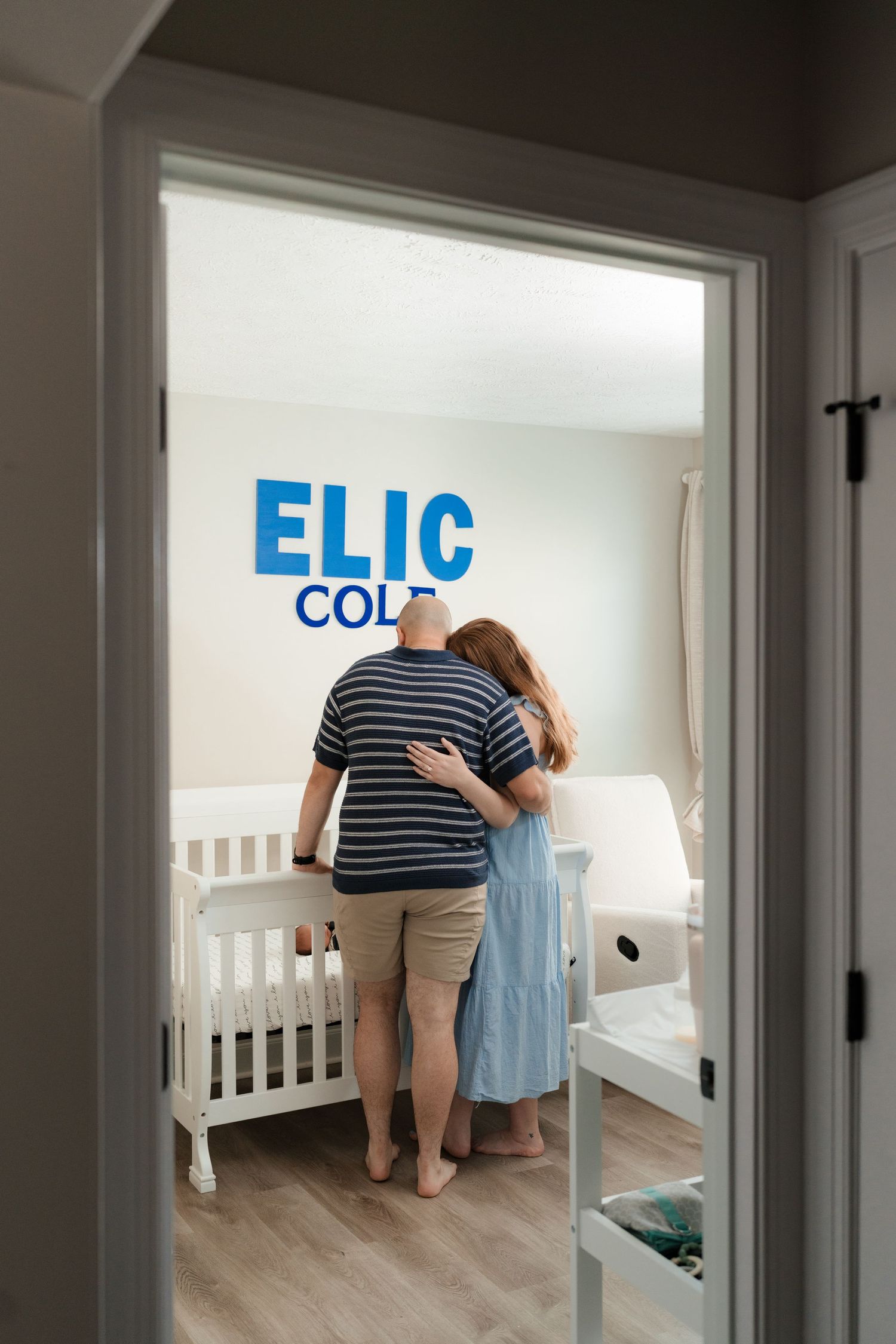 Two people decorating a nursery room with blue lettering on white walls for a fresh 48 family nursery session.