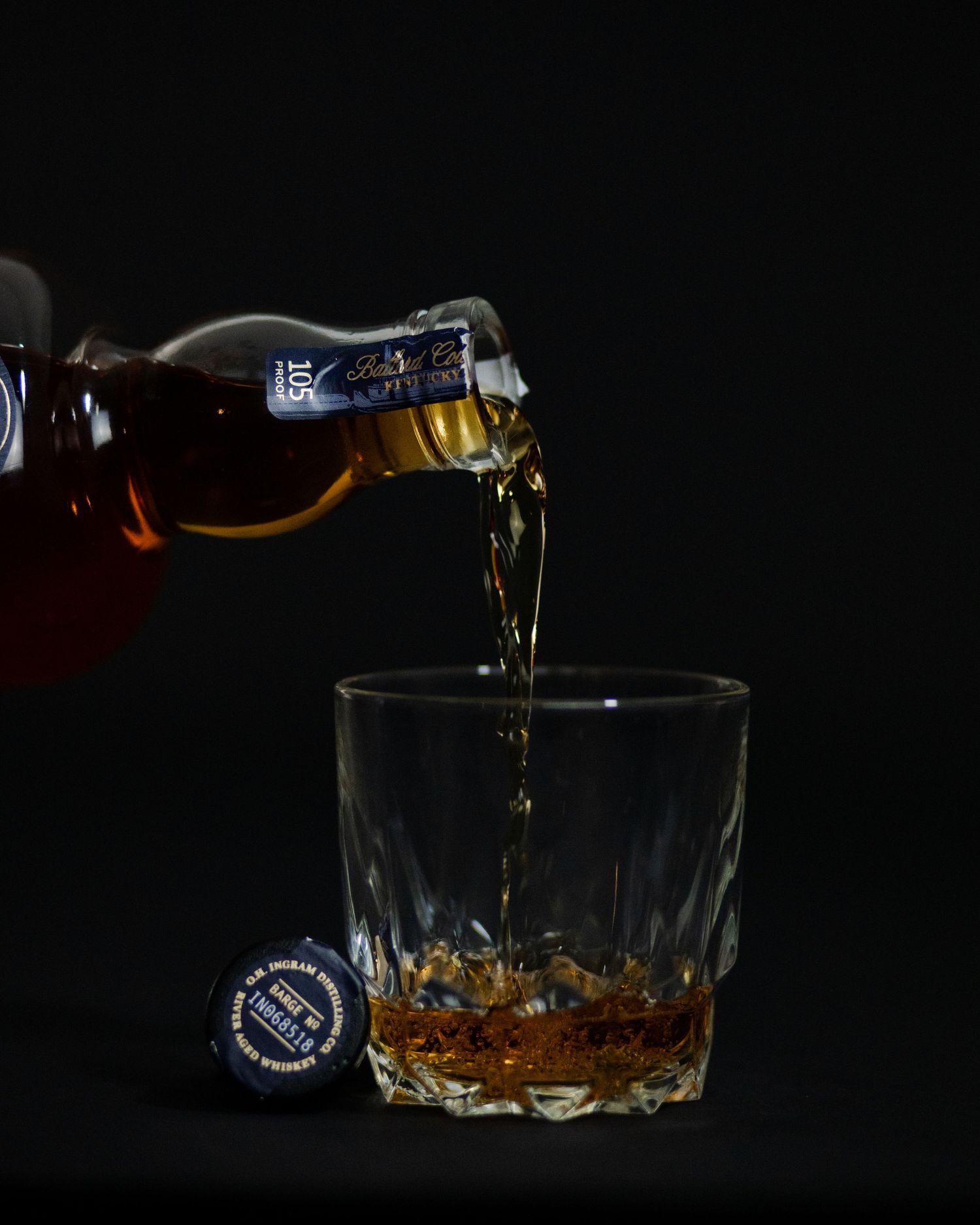 Product photography of OH Ingram River Aged Bourbon being poured into crystal glass against dark background.