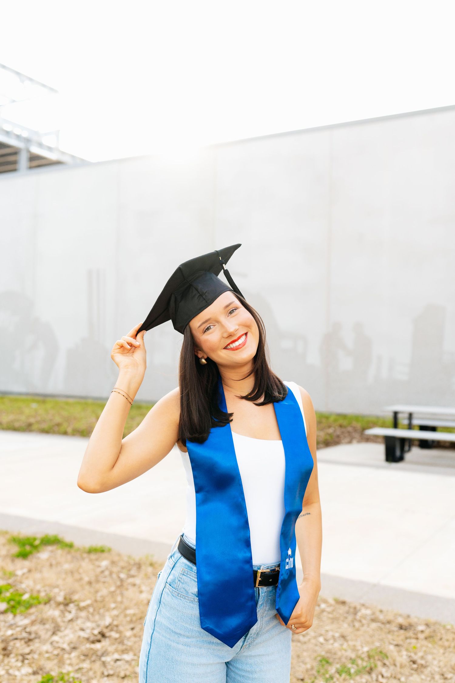 Graduate in blue stole and cap celebrates against white building background.
