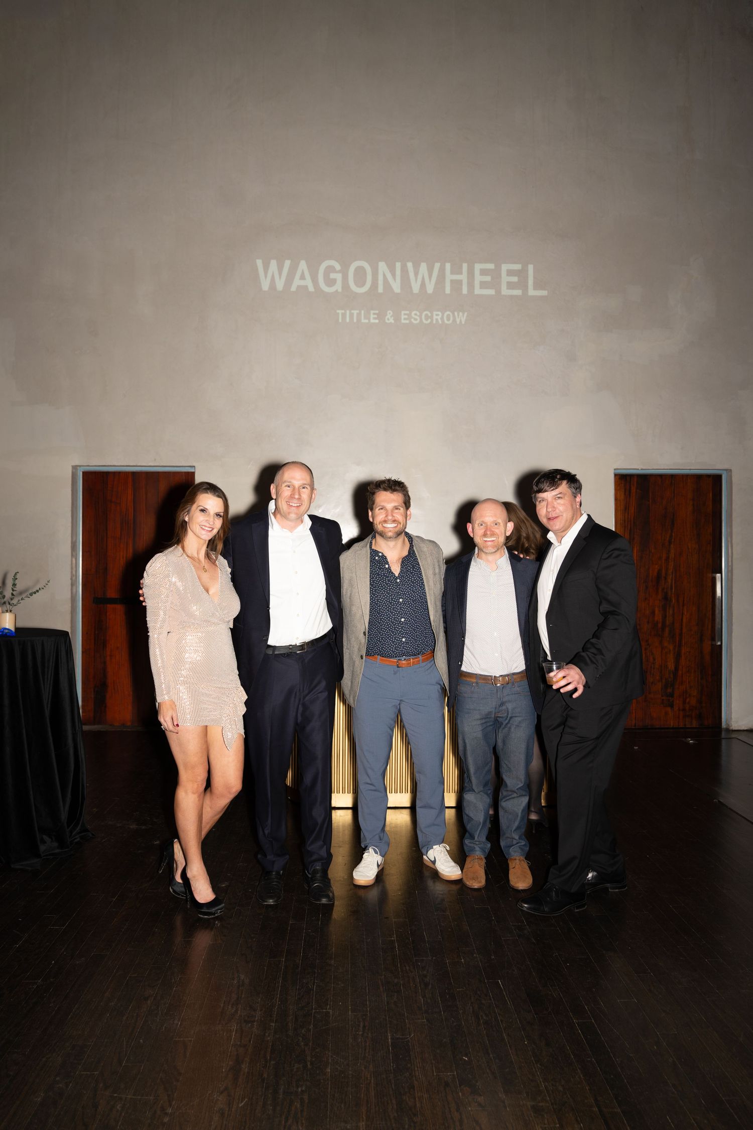 A group of performers lined up against a dark wall with Wagonwheel text visible in a theatrical setting.