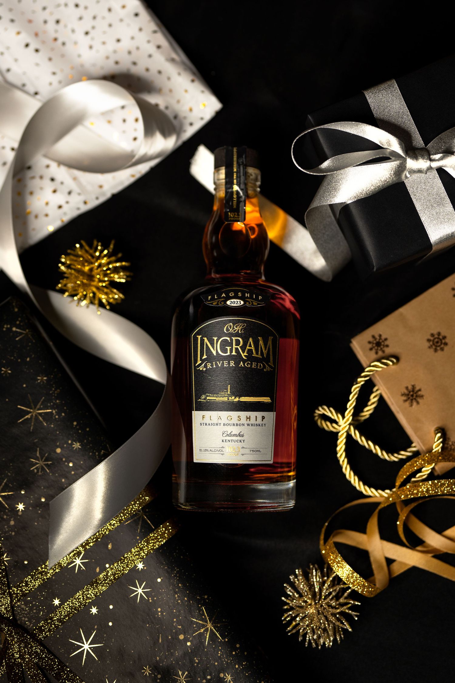 Product photography of OH Ingram River Aged Whiskey bottle display with gold decorations and white ribbons on black background.