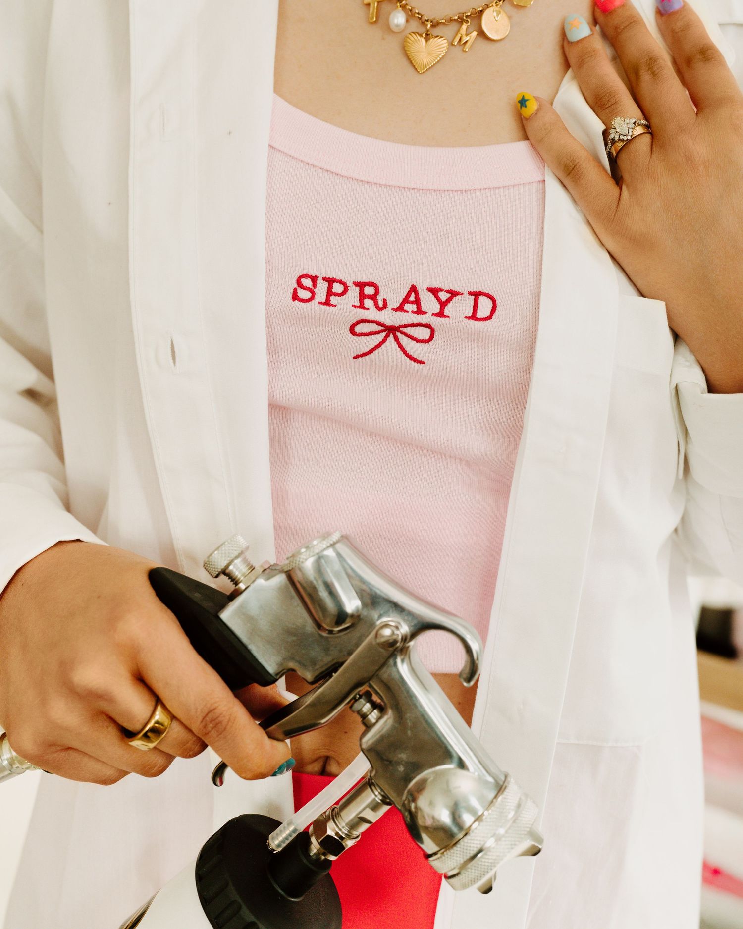 Close-up of hands holding silver spray tan sprayer for SPRAYD branding.