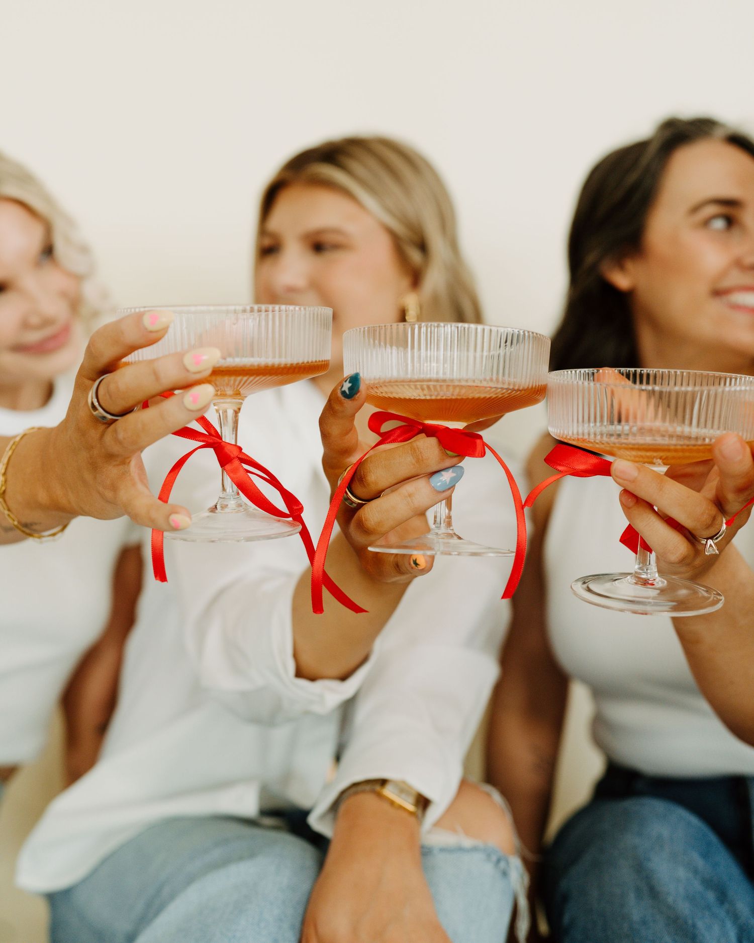 Group enjoying drinks with red ribbons on champagne glasses. Studio branding photoshoot for small business. tanning inspo.