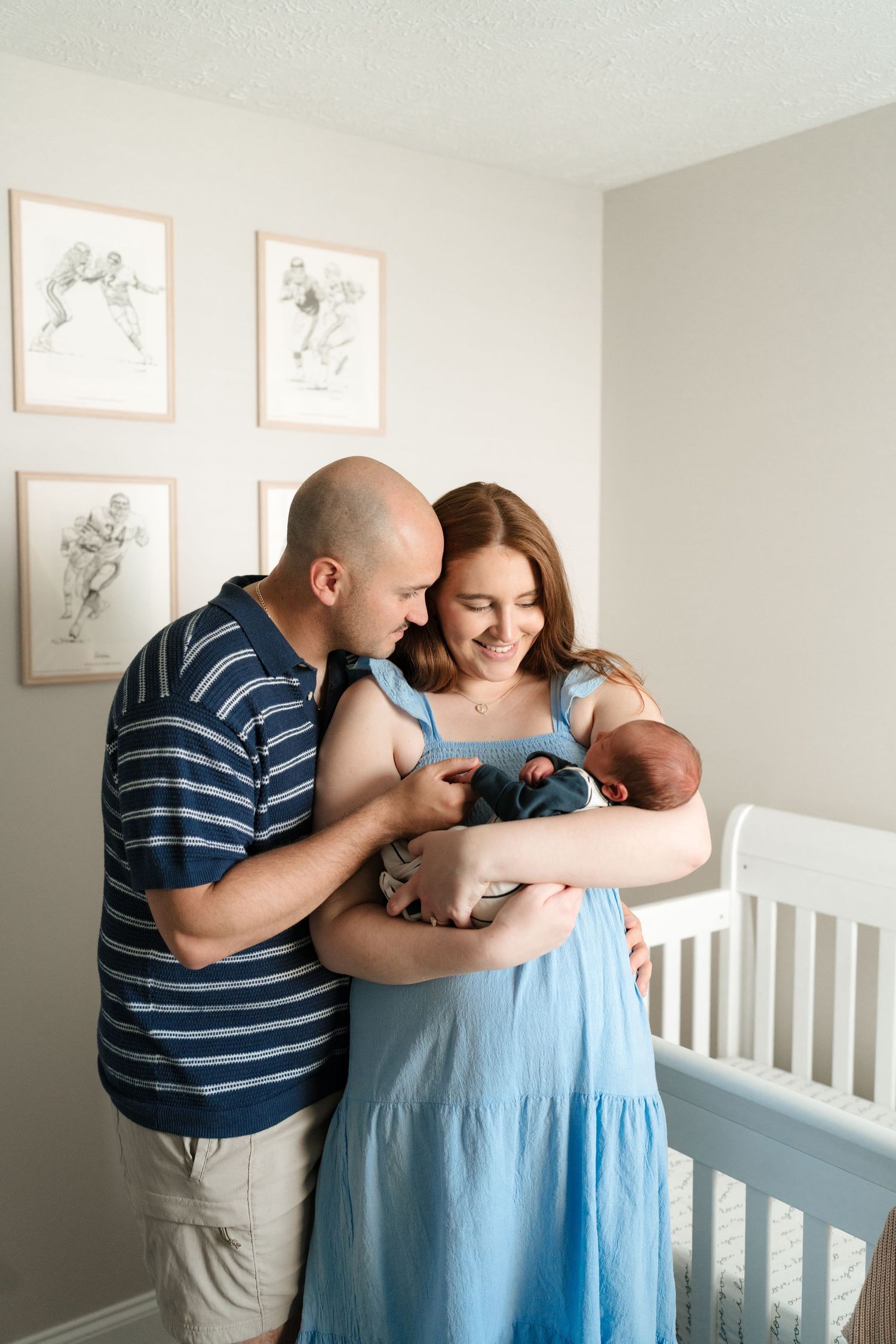 A couple in blue and striped clothing share tender moments with their newborn baby in a nursery setting.