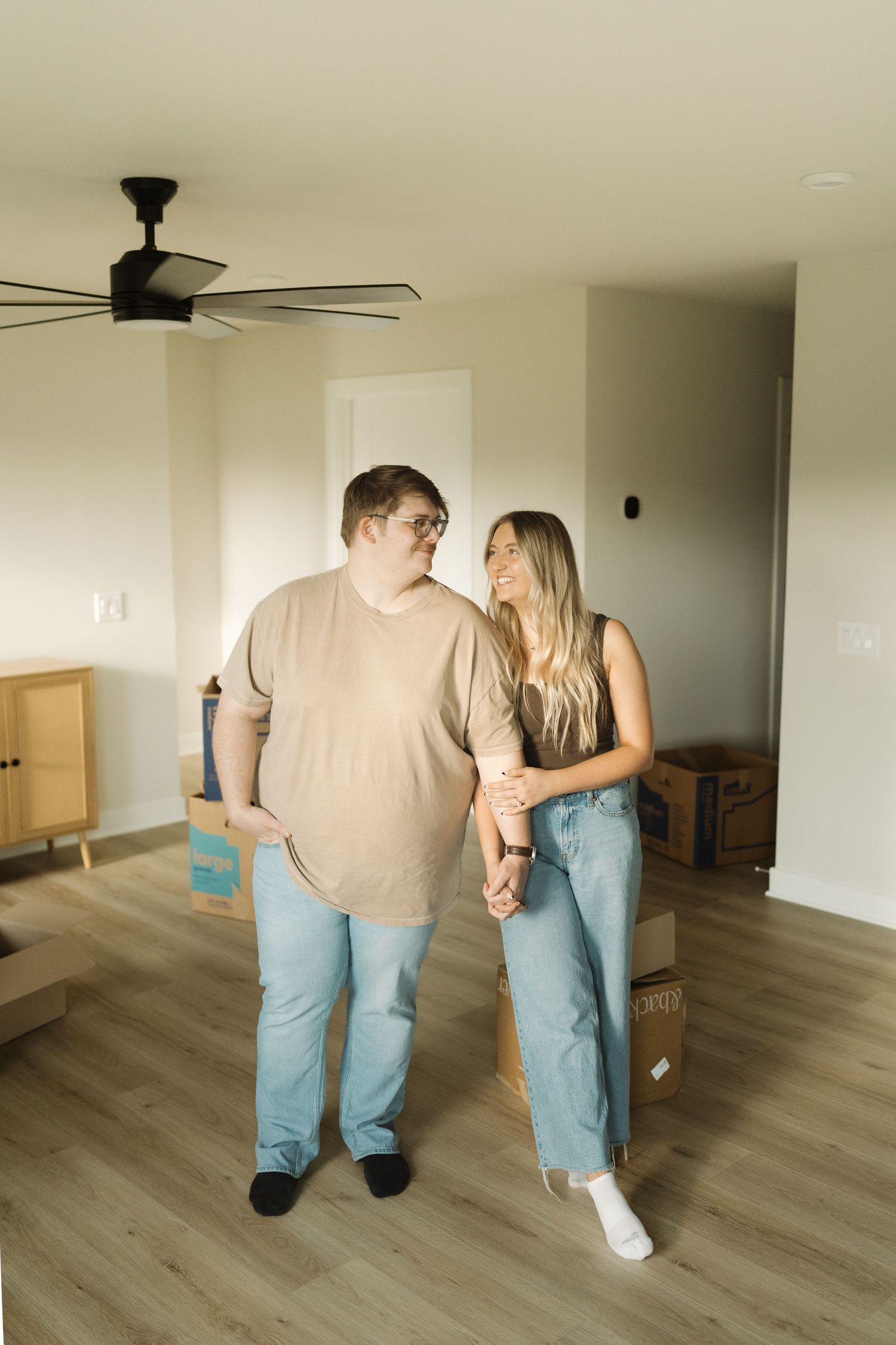 A couple walks together across an empty room with light hardwood floors and white walls in a sequence of photos.