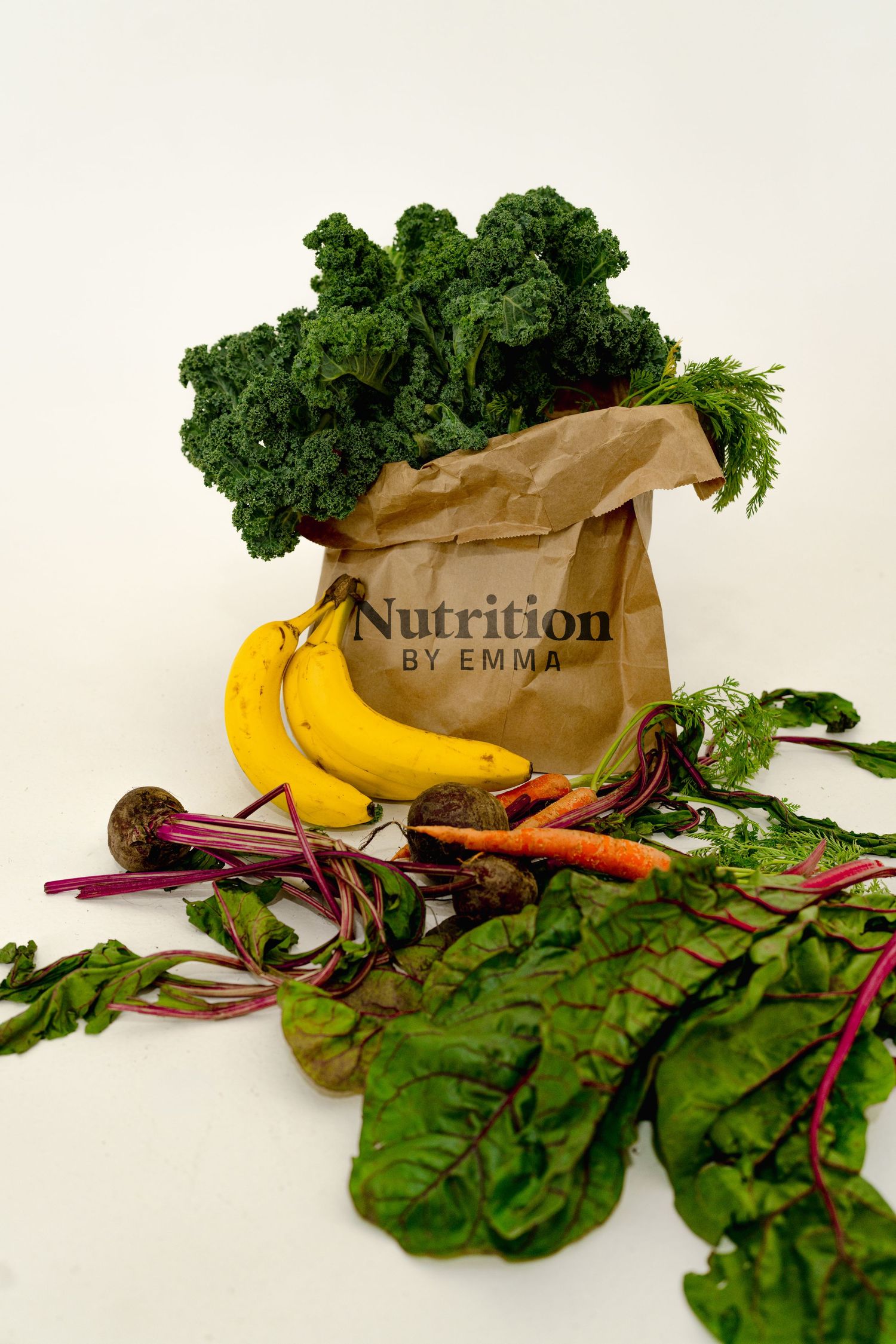 Fresh produce arrangement with kale, bananas and nutrition text on brown paper bag. Branding for nutrition by emma.