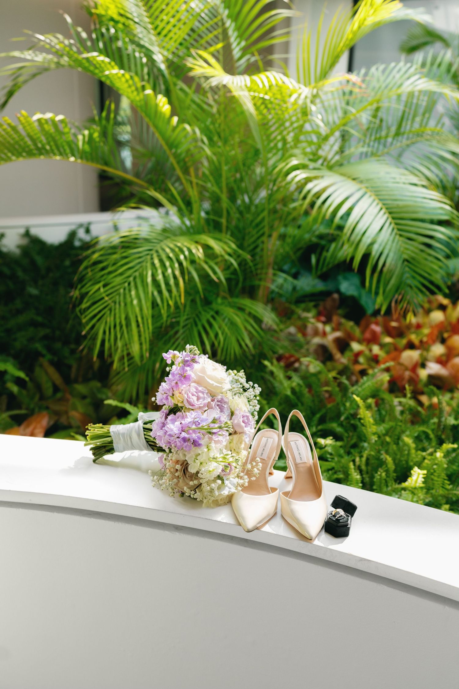 Bridal accessories displayed on white ledge with tropical palm leaves in background at cheekwood in nashville.