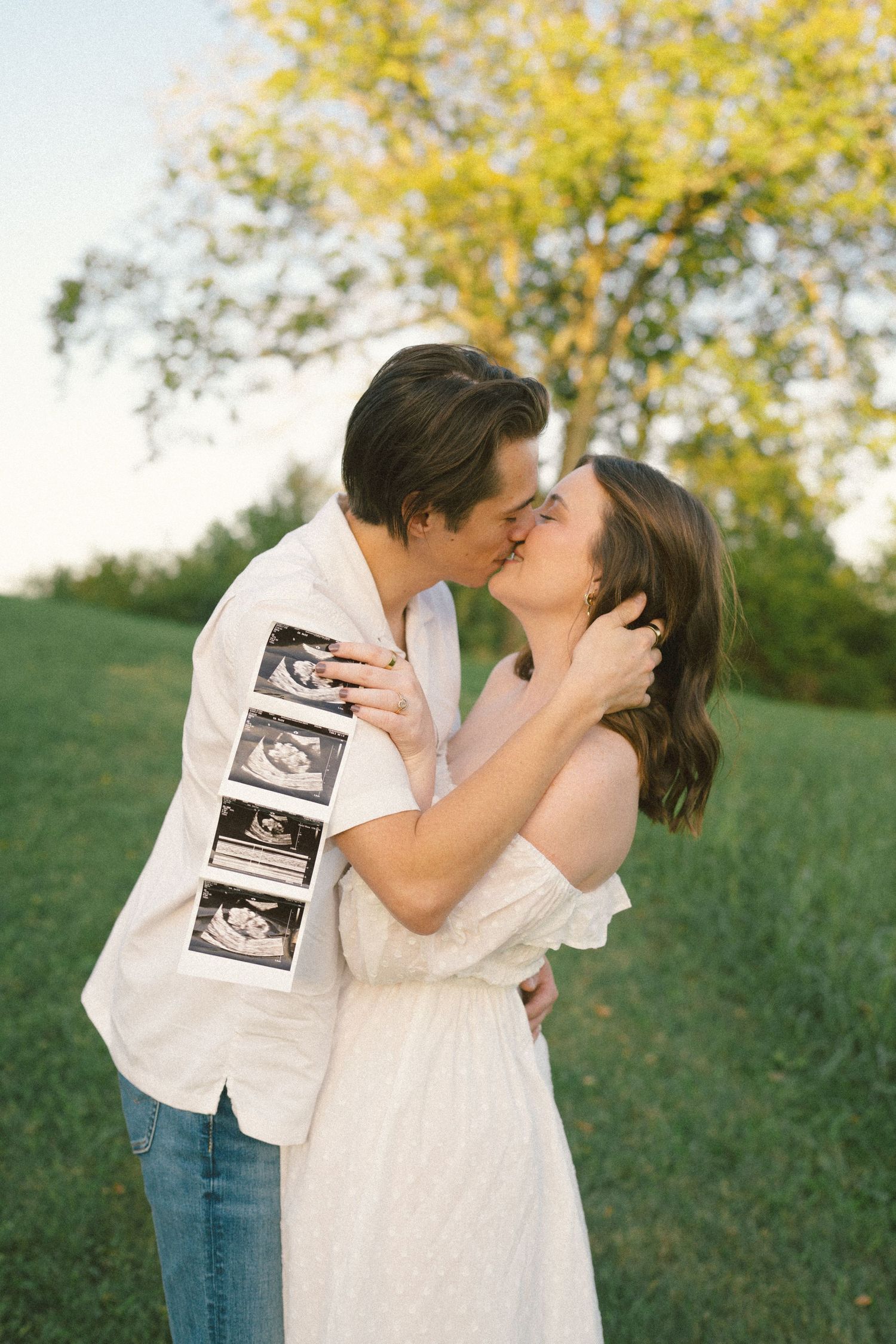 A couple kisses while holding ultrasound photos in a sunny outdoor setting in Franklin TN.