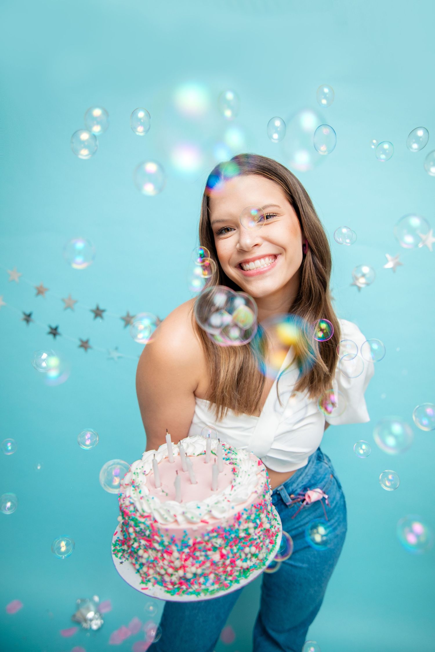 Playful scene with bubbles and confetti against a turquoise background with cake for birthday photoshoot.