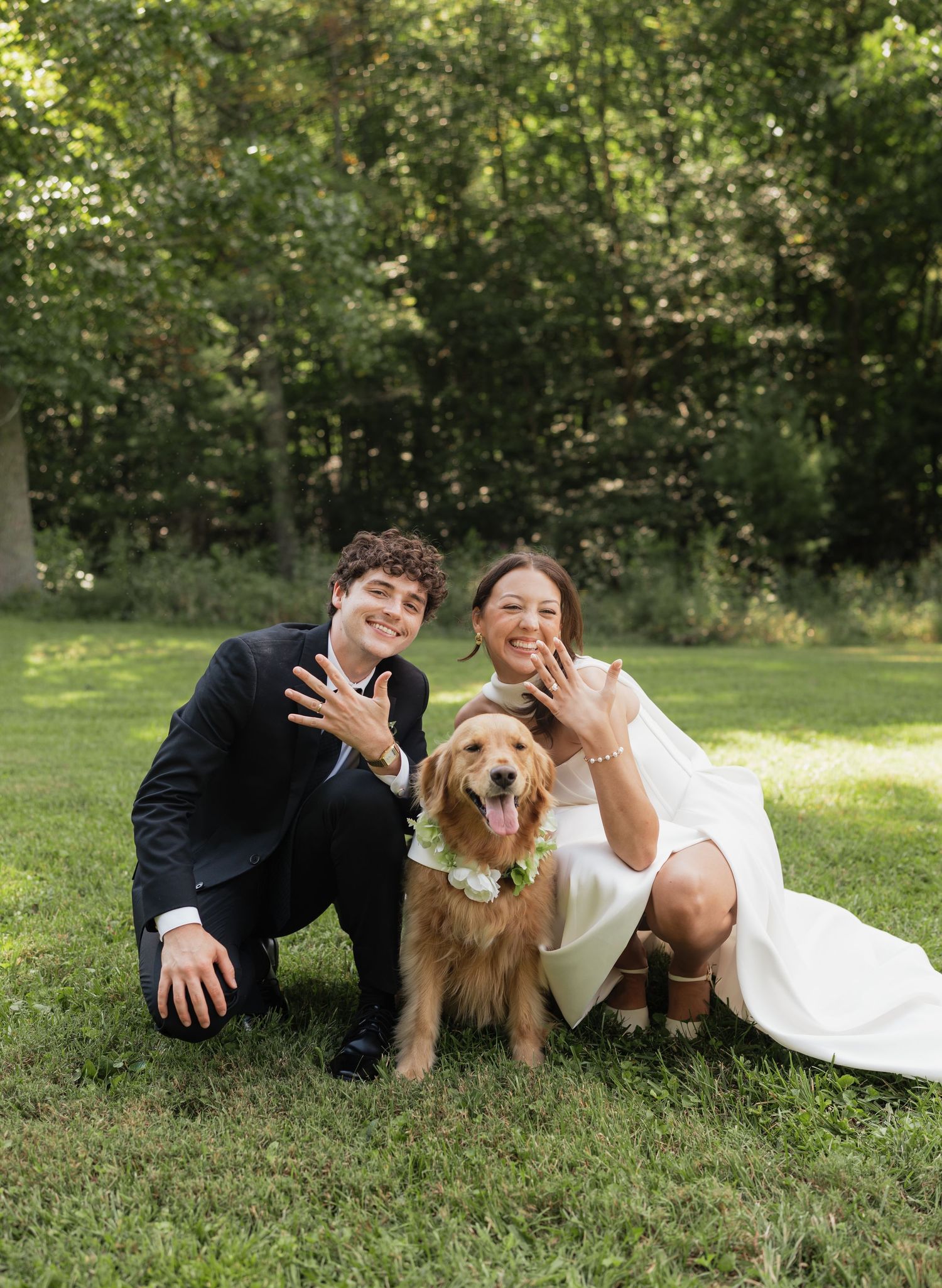 A couple lying in grass with their golden retriever enjoying a sunny day in a park setting.