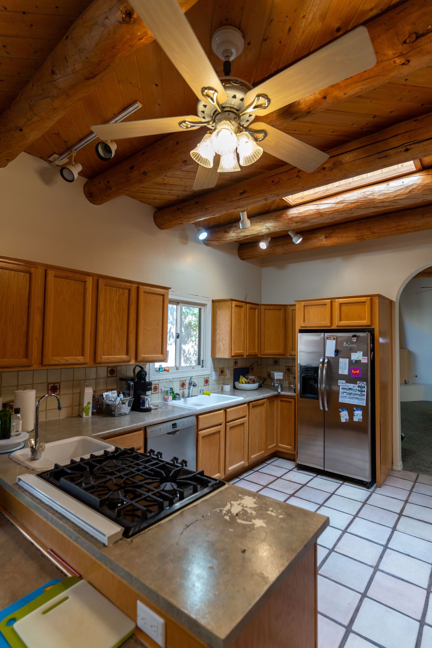 Modern kitchen with exposed wooden beams, gas stove, stainless steel appliances, and light wood cabinets.