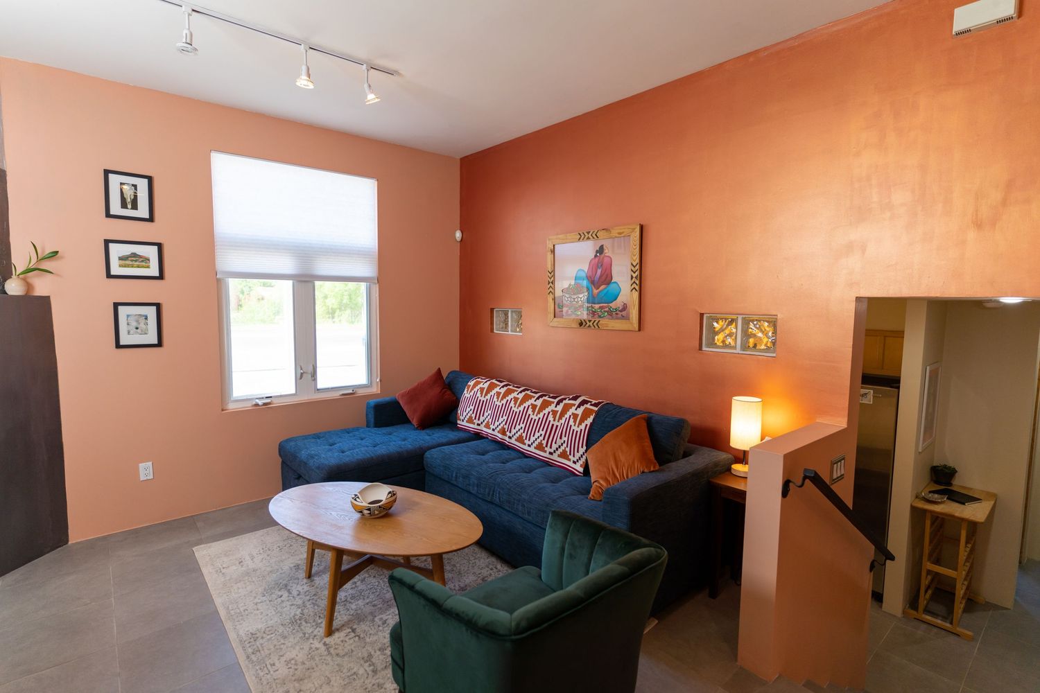 Modern living room with peach walls features a blue sofa, green accent chair, and wooden coffee table in a cozy setup.