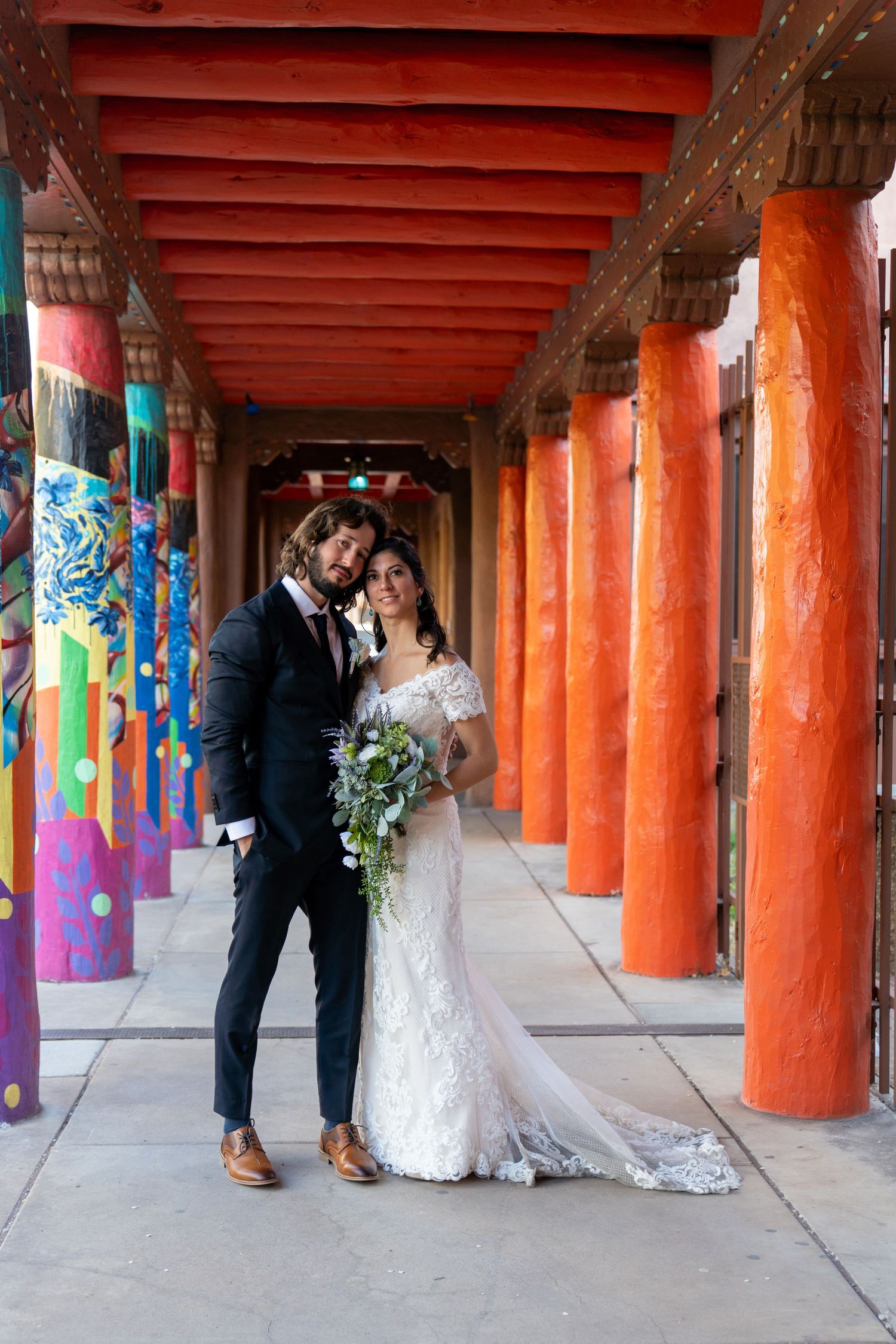 A couple sharing an intimate moment in a colorful covered walkway with bright orange pillars and painted murals.