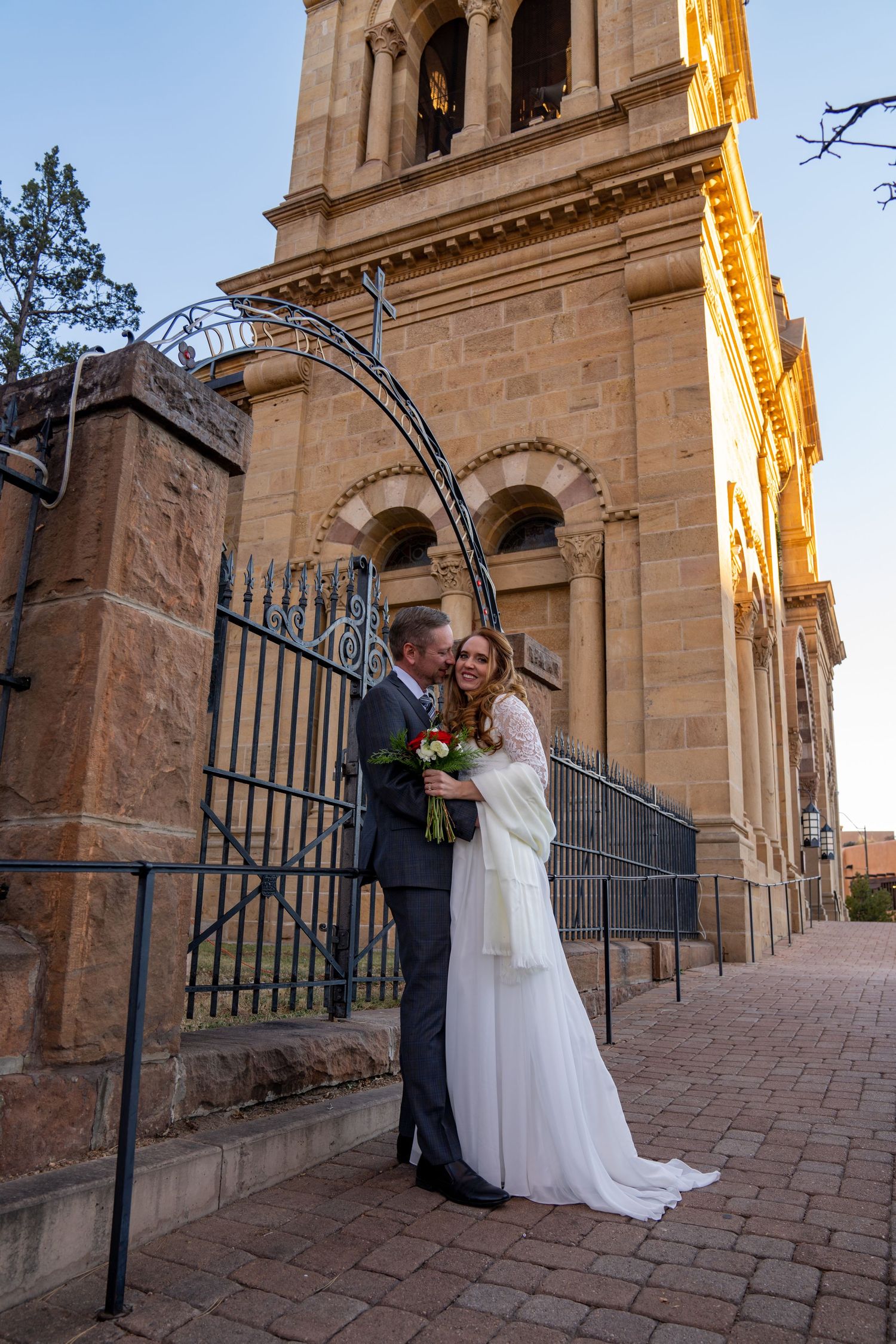 Bride and groom share romantic moments outside historic stone church with ornate architecture and iron gates.