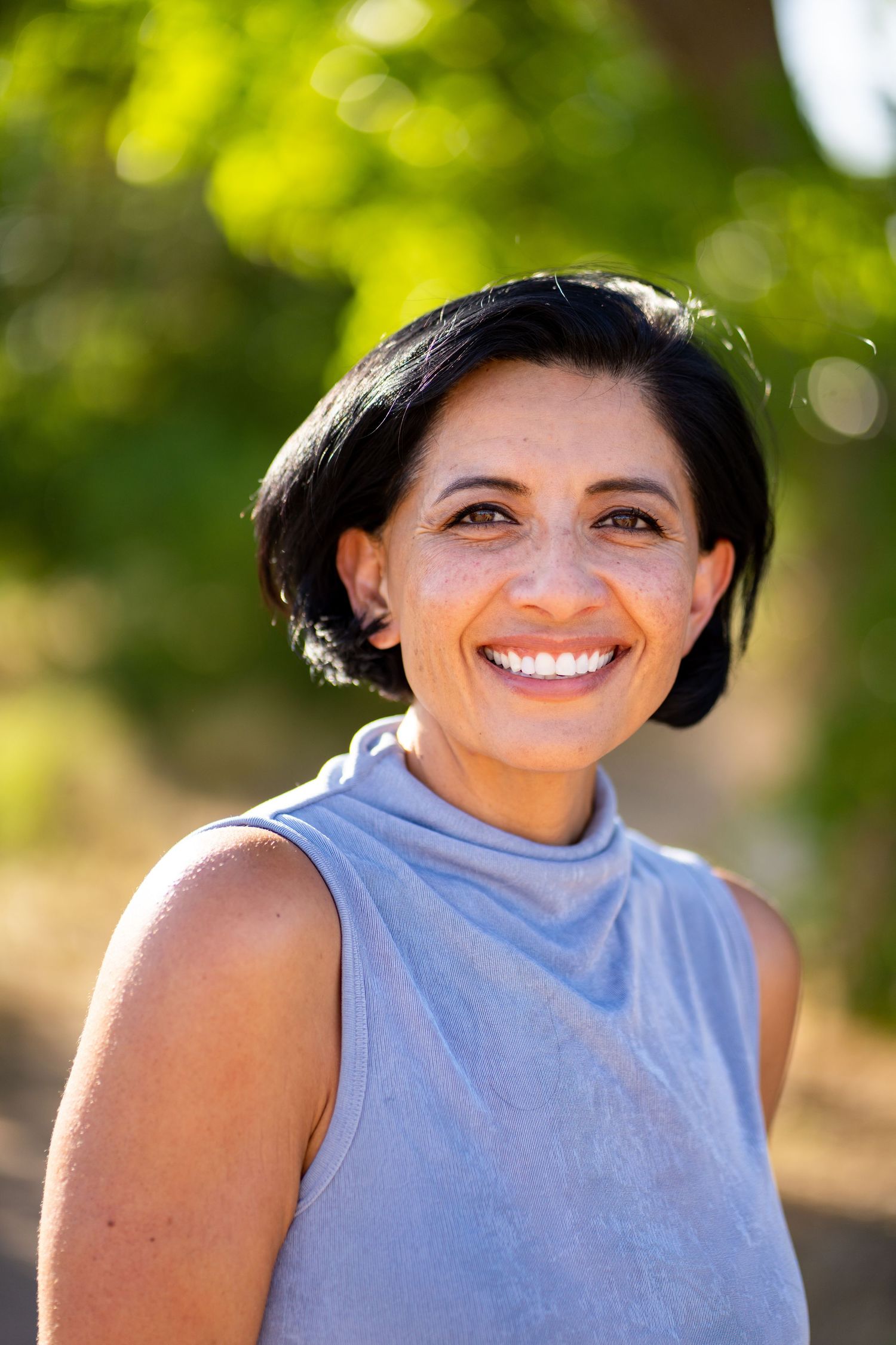 Person in light blue sleeveless top smiling outdoors.