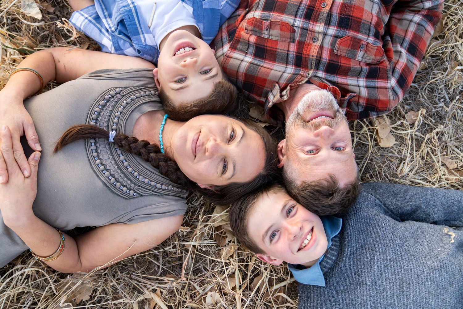 Family lying on dry grass in a circle formation looking up at camera.